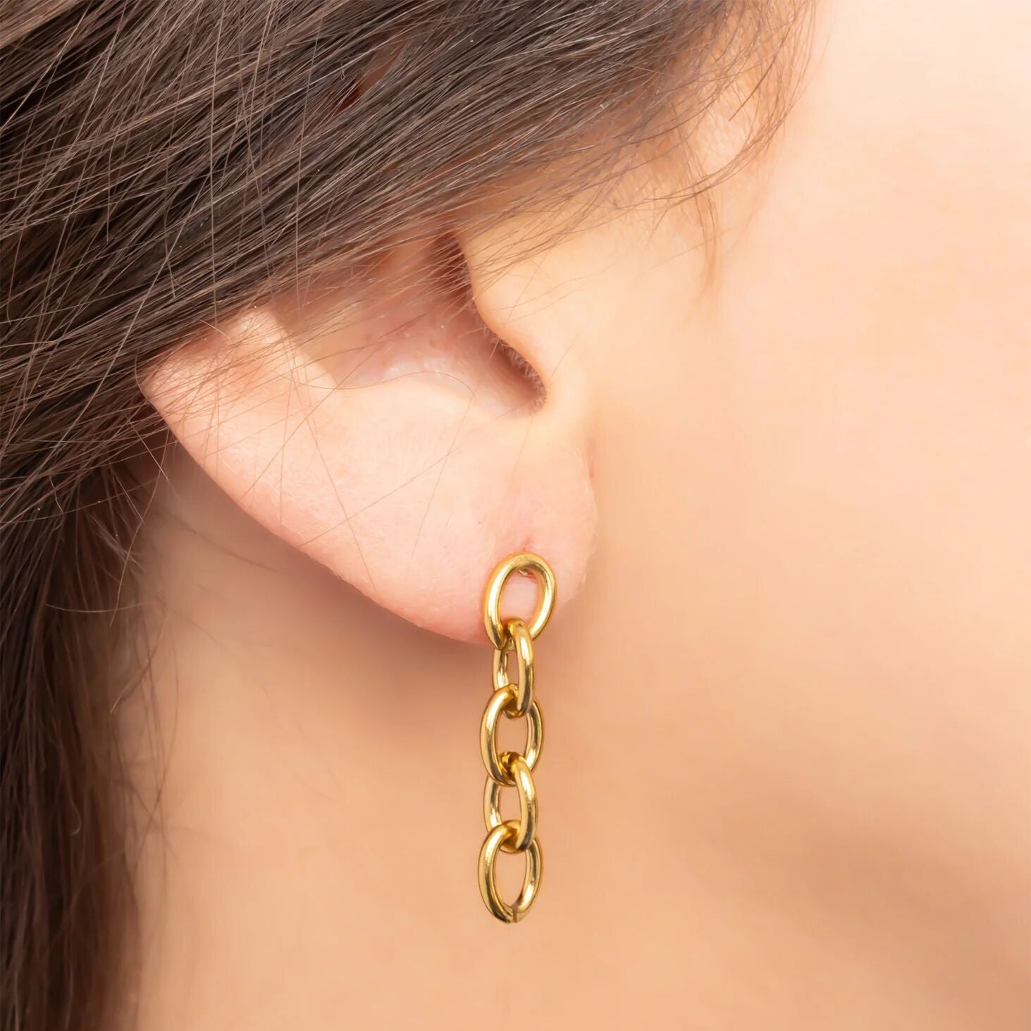 Gold chain earring worn by a person with a neutral background
