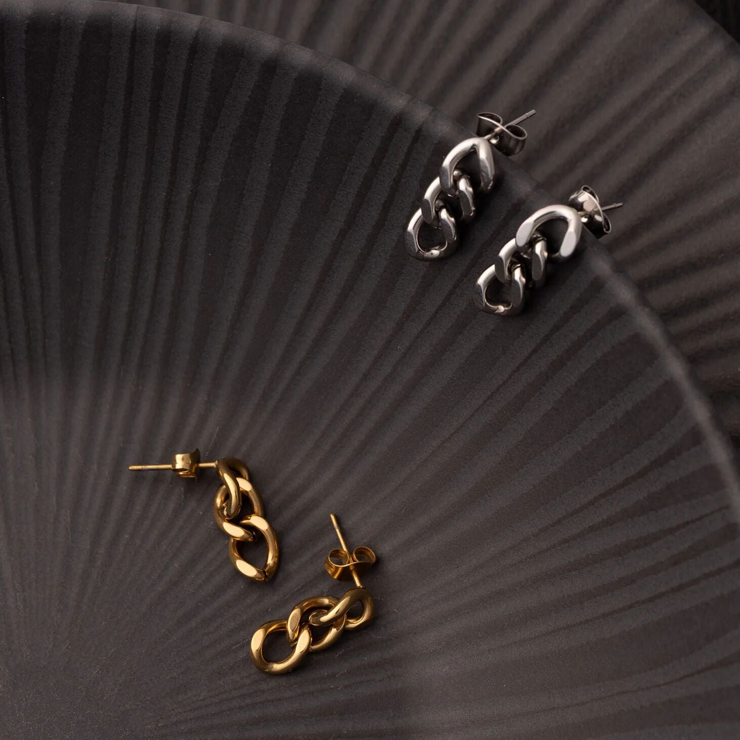 Pair of gold and silver chain-style earrings on a textured dark surface