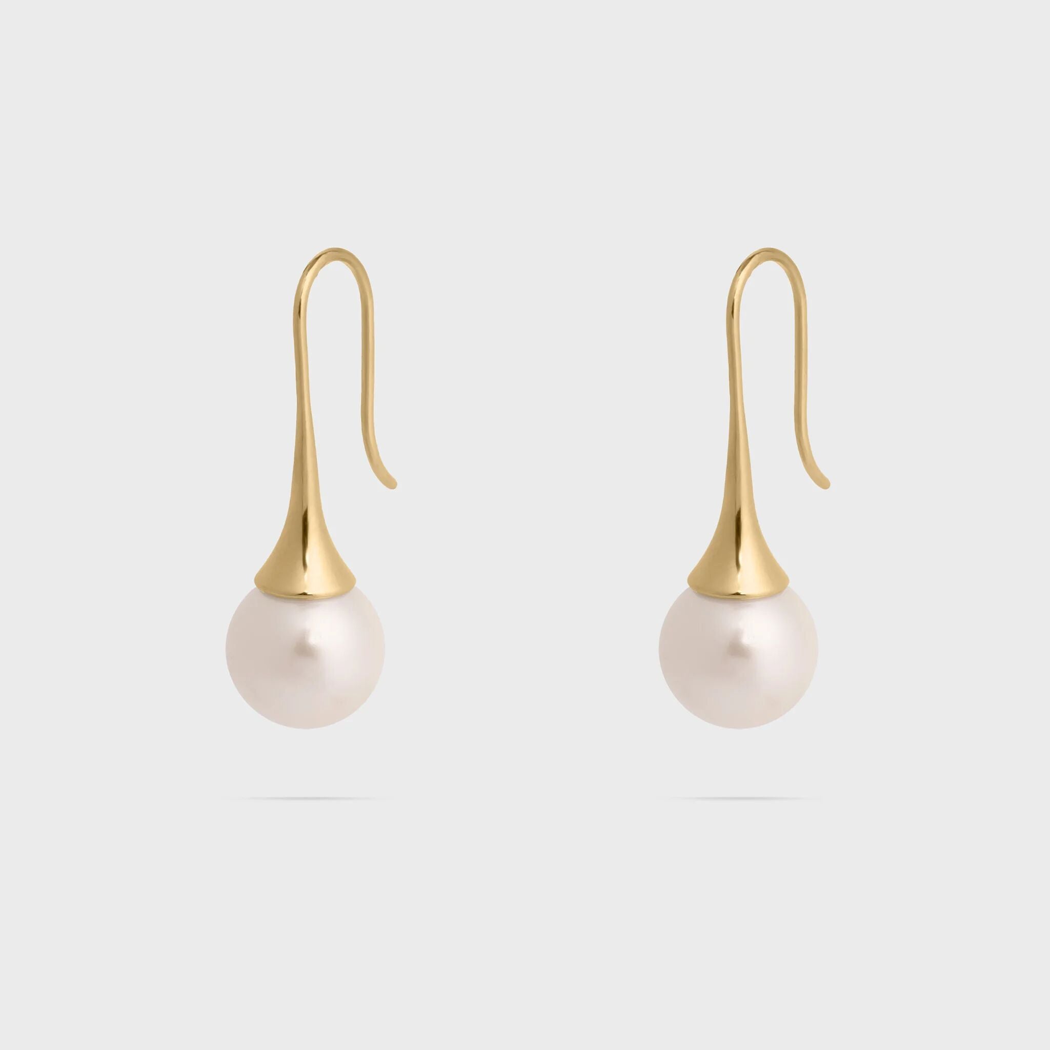 Pair of pearl earrings with gold hooks on a light gray background