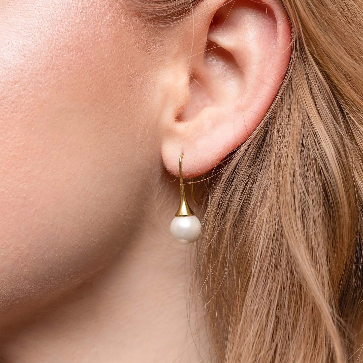 Close-up of an ear wearing a pearl earring with a gold hook.