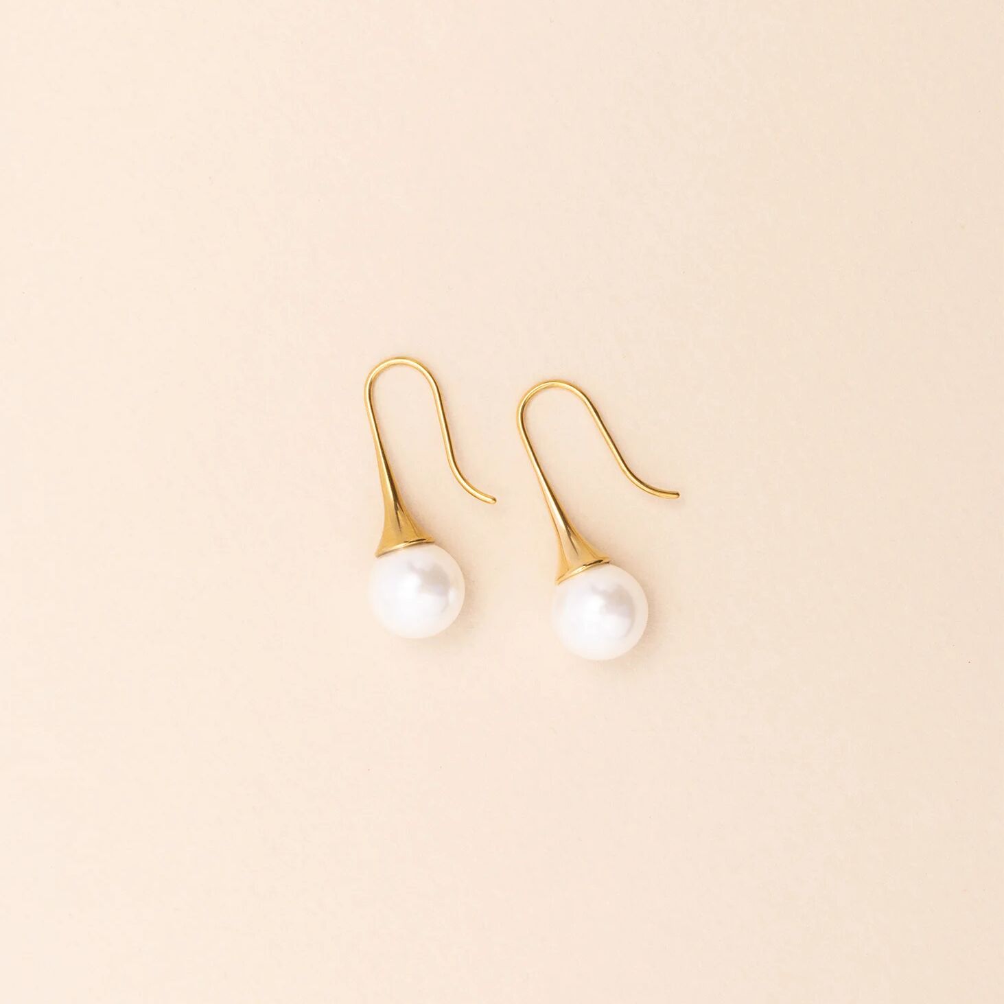 Gold earrings with pearl drops on a beige background