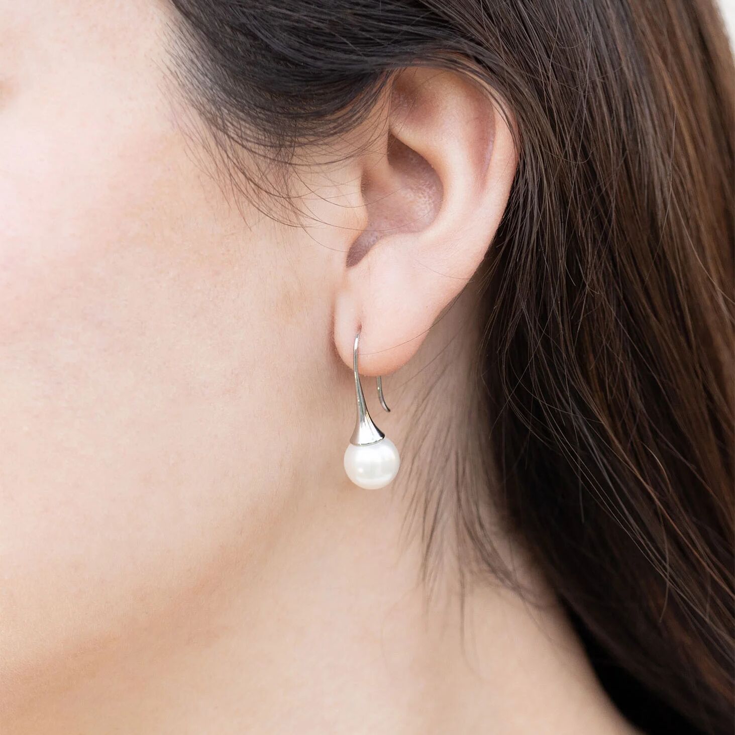 Pearl earring worn by a person with dark hair.