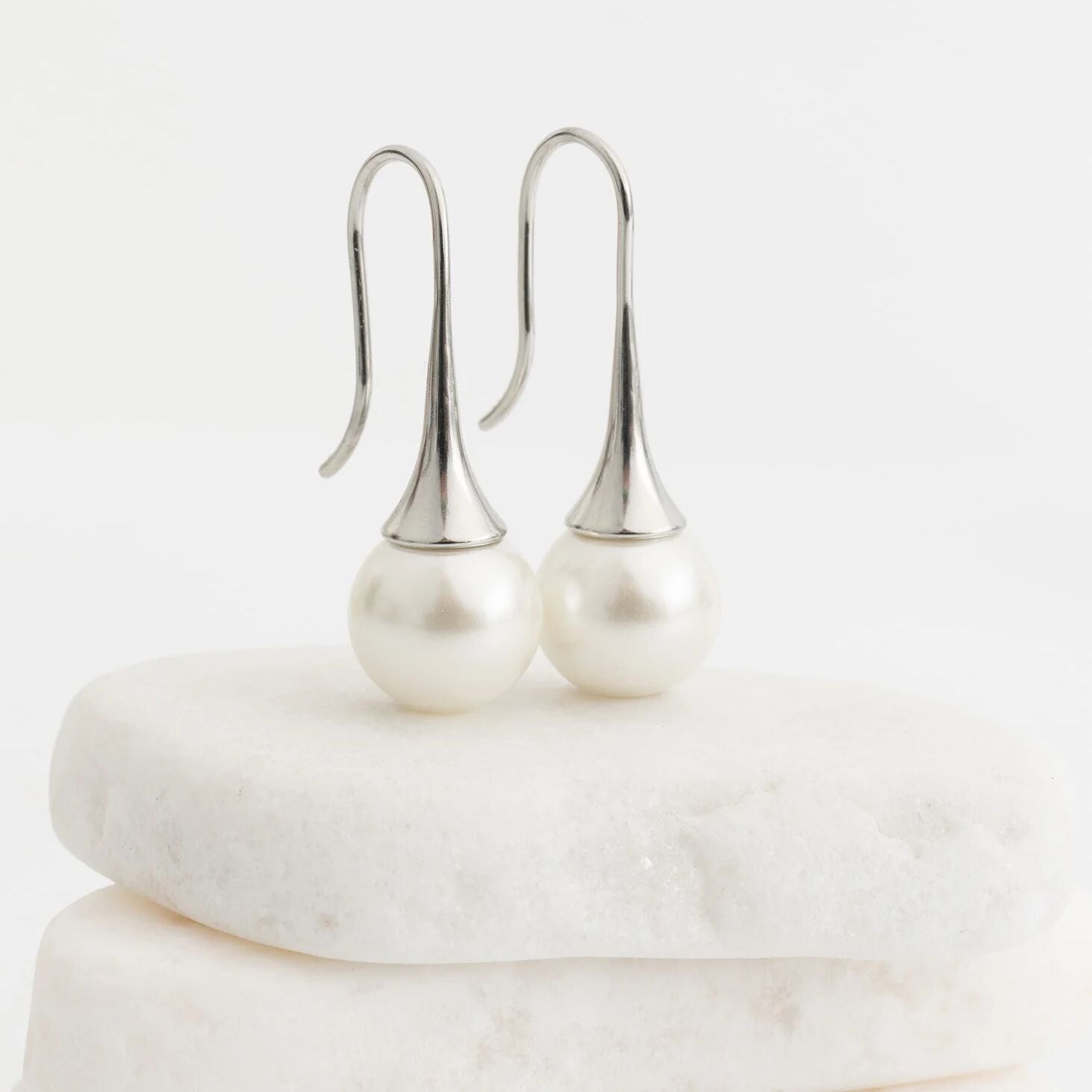 Pearl earrings on a white marble surface with a light gray background