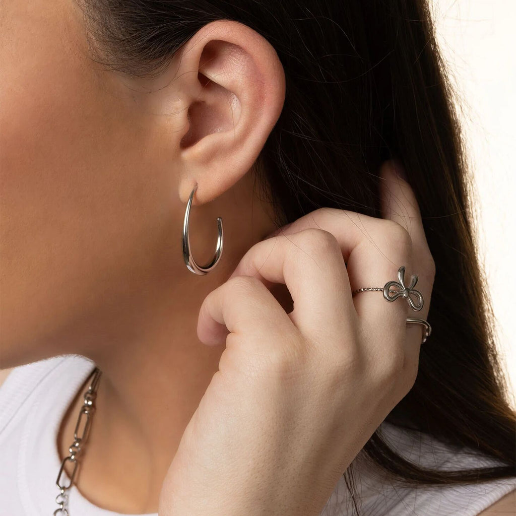 Close-up of a person wearing silver hoop earrings and a ring, with a neutral background.