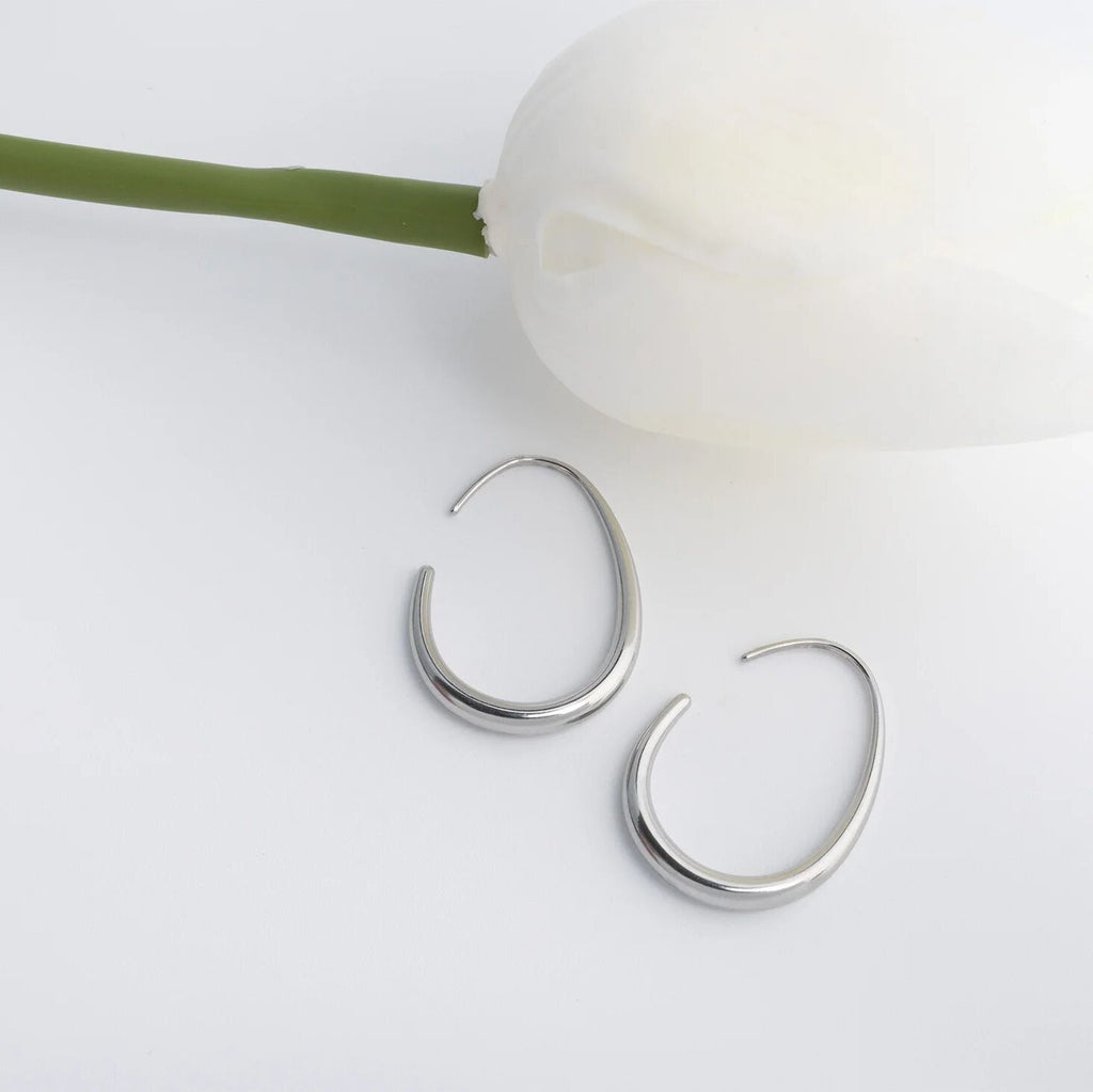 Silver hoop earrings on a light surface with a white flower and green stem.