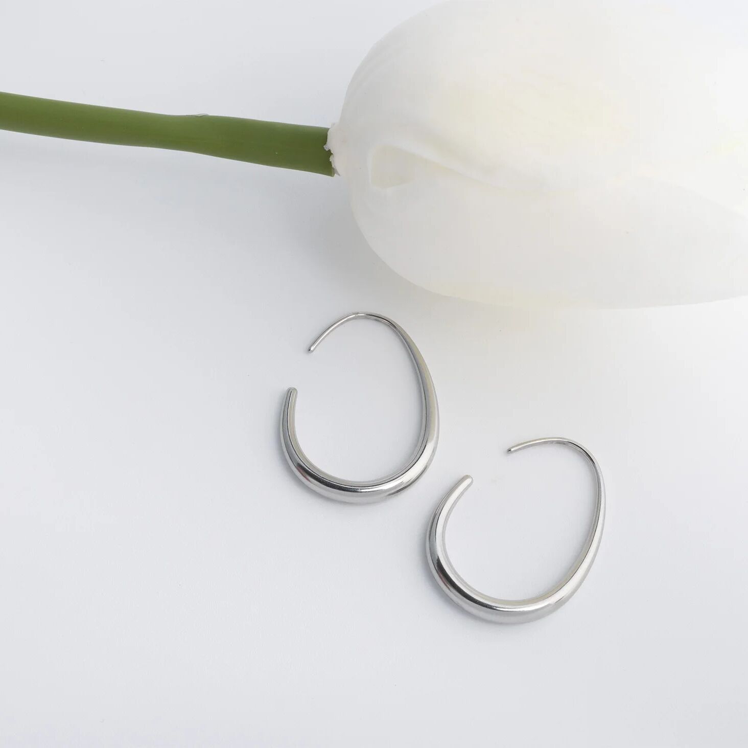Silver hoop earrings on a light surface with a white flower and green stem.