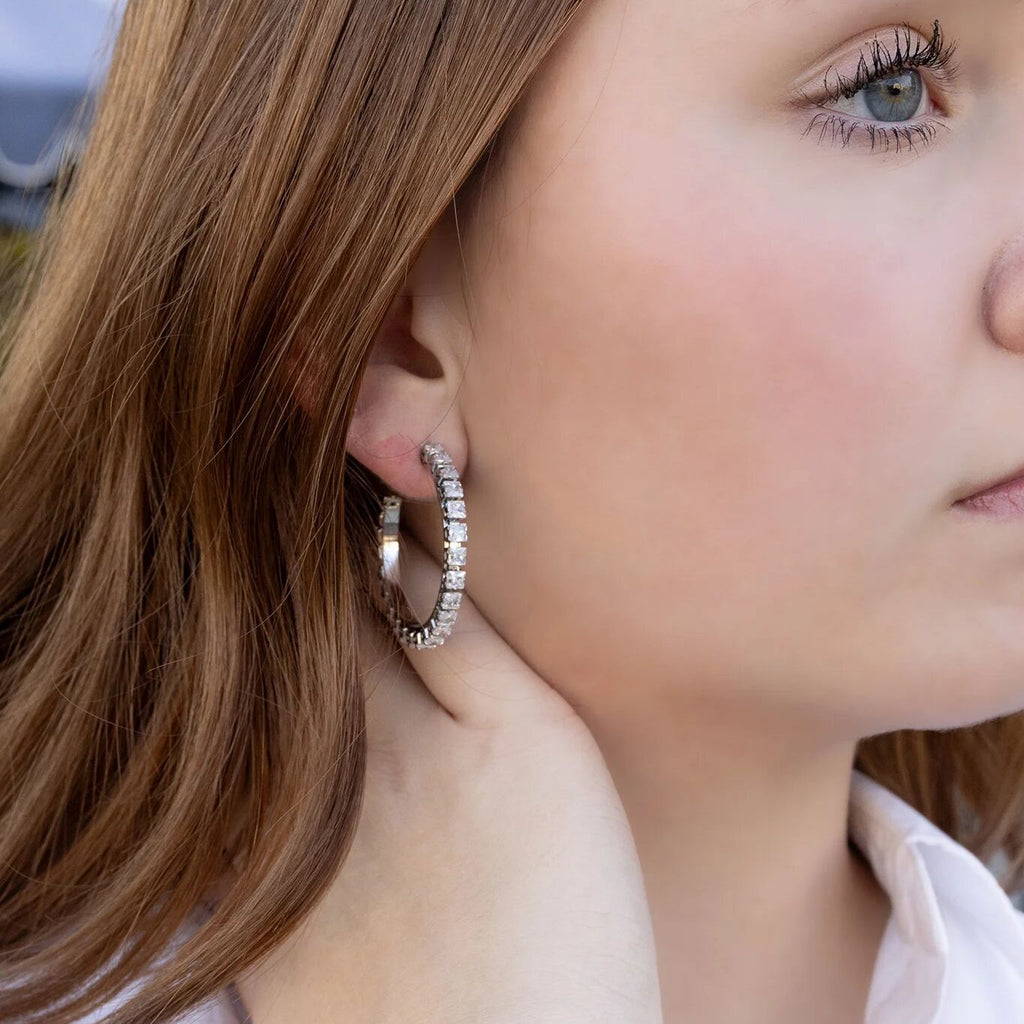 Close-up of a person wearing silver hoop earrings with a blurred background
