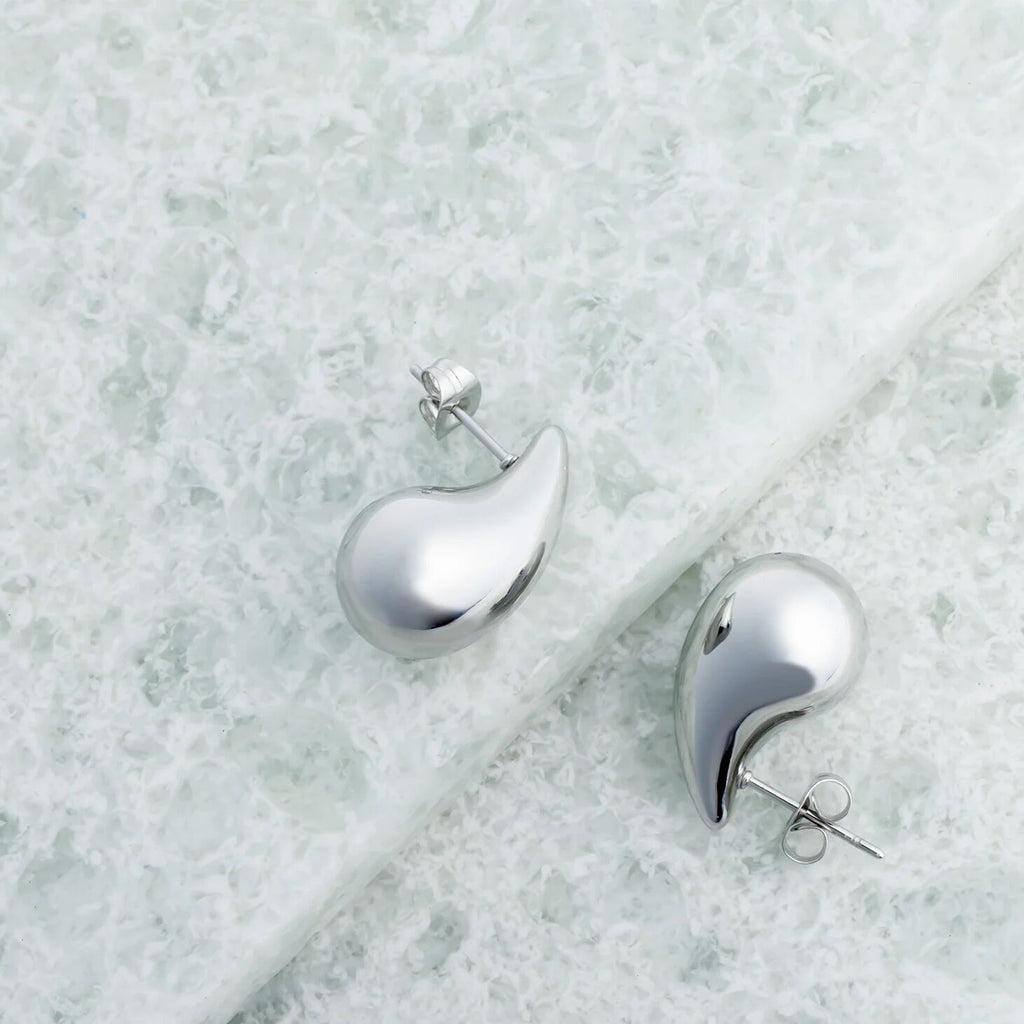Silver teardrop-shaped earrings on a light marble surface