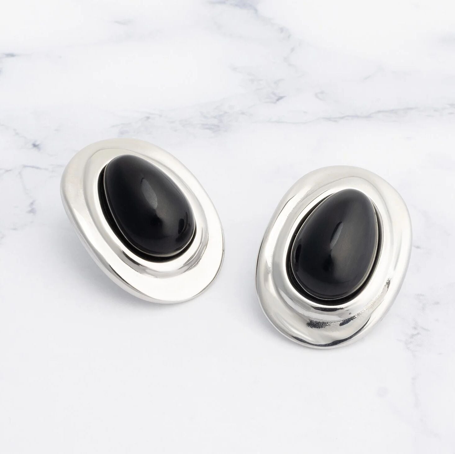 Pair of silver Black Enamel Stud Earrings with black stones on a marble surface