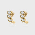 Gold Oval Stone Huggie Earrings with clear gemstones on a light gray background