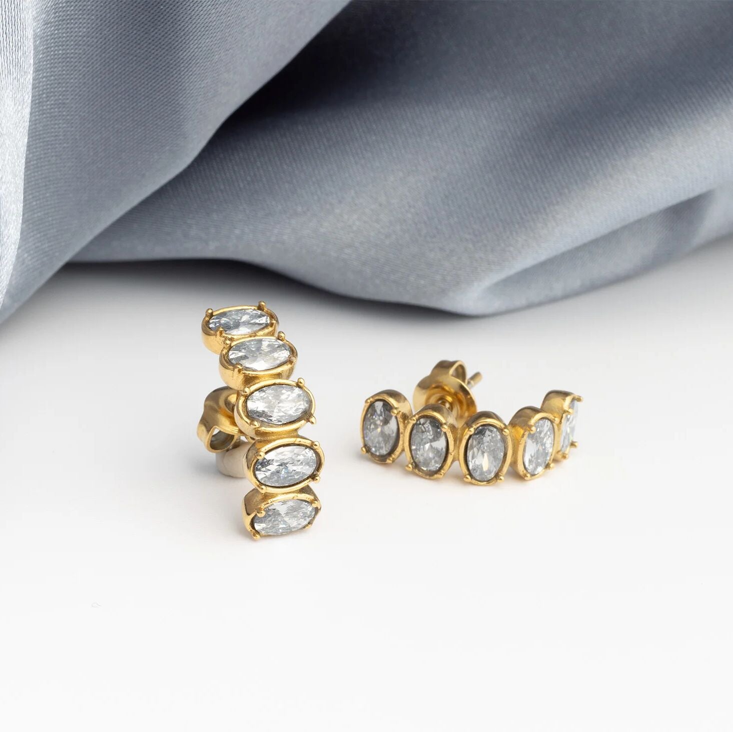 Gold Oval Stone Huggie Earrings with clear stones on a light gray fabric background