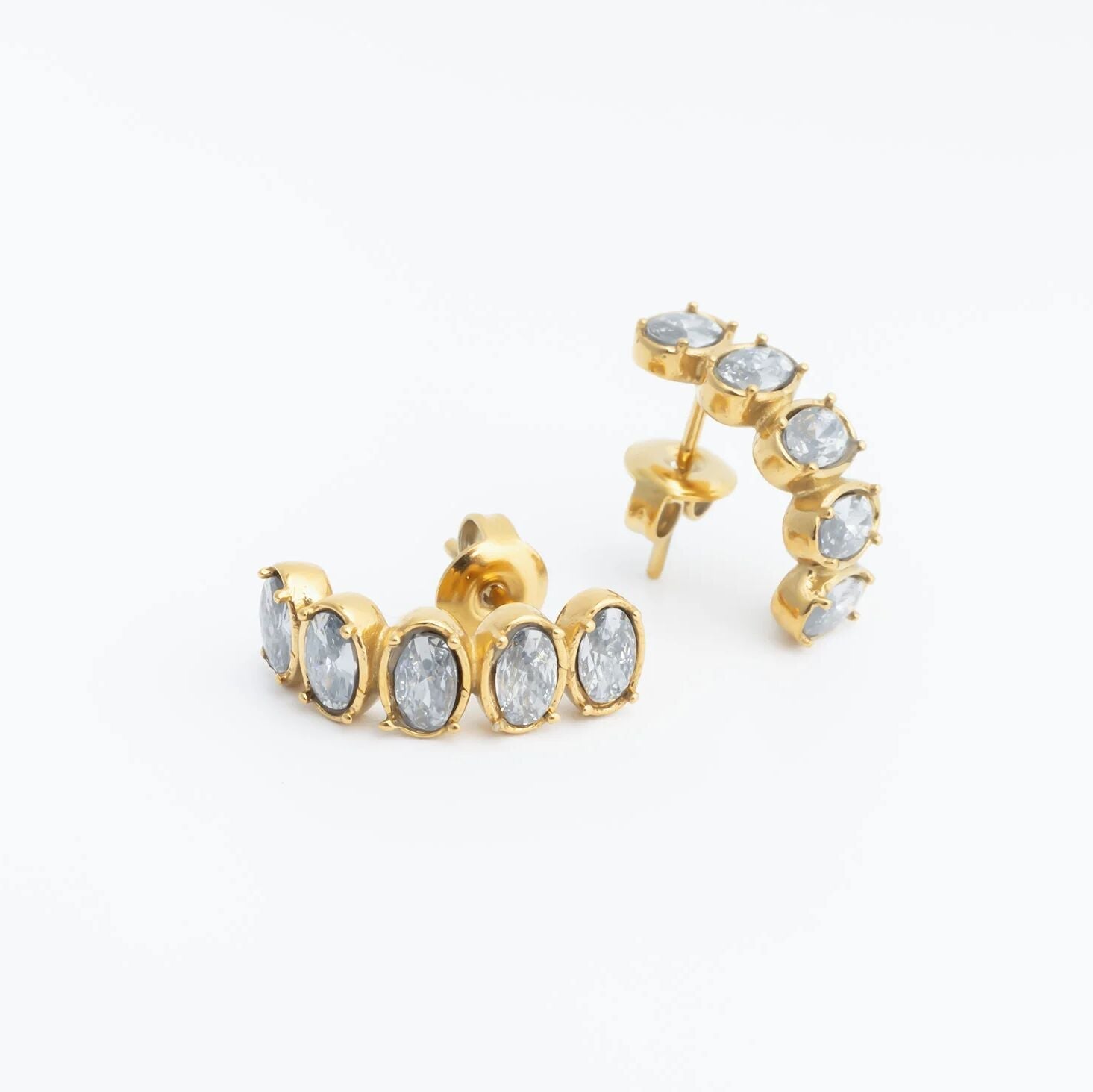 Gold hoop Oval Stone Huggie Earrings with clear gemstones on a white background