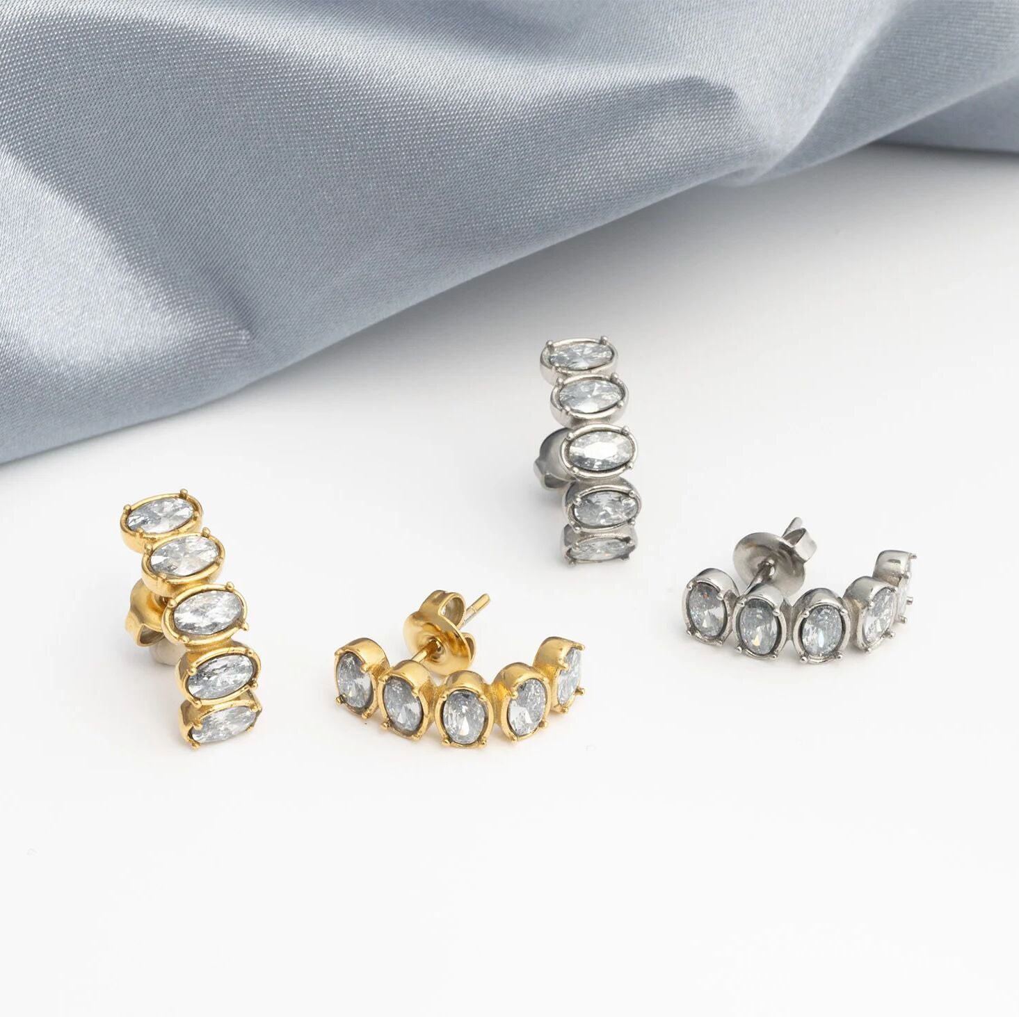 Gold and silver hoop Oval Stone Huggie Earrings on a light gray fabric background