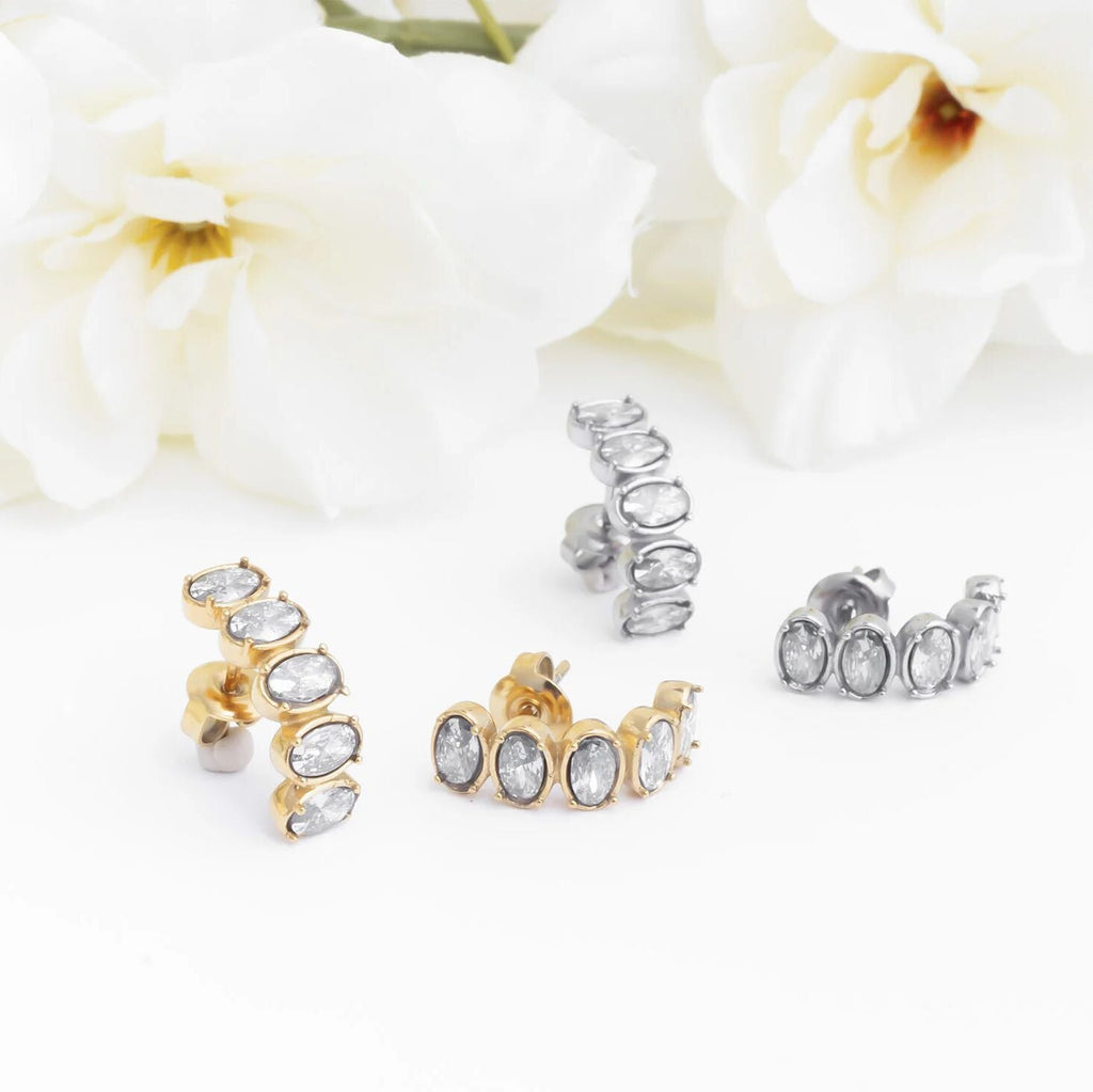Gold and silver stud Oval Stone Huggie Earrings on a white background with flowers.