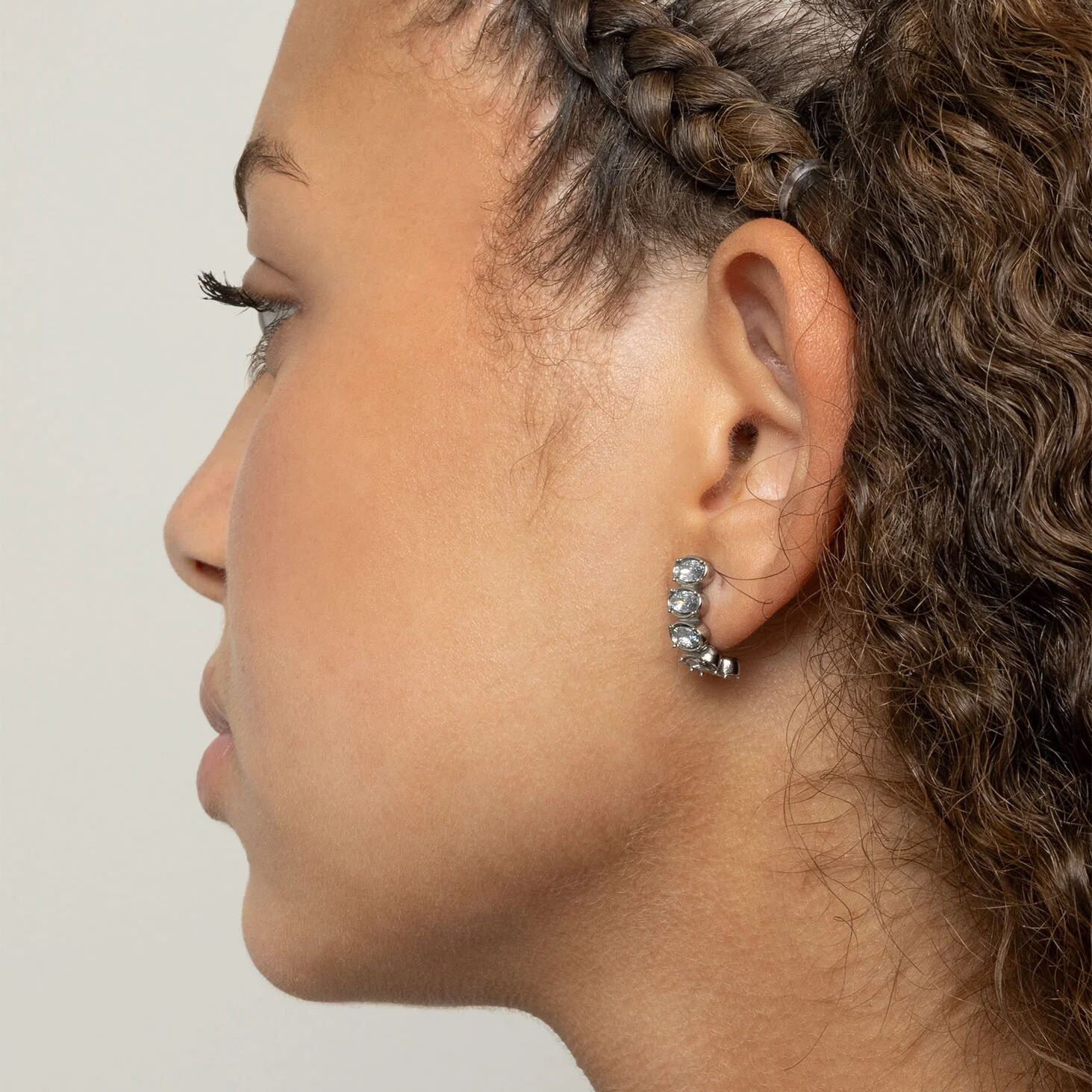 Close-up of a person wearing a silver hoop Oval Stone Huggie Earrings with a plain background