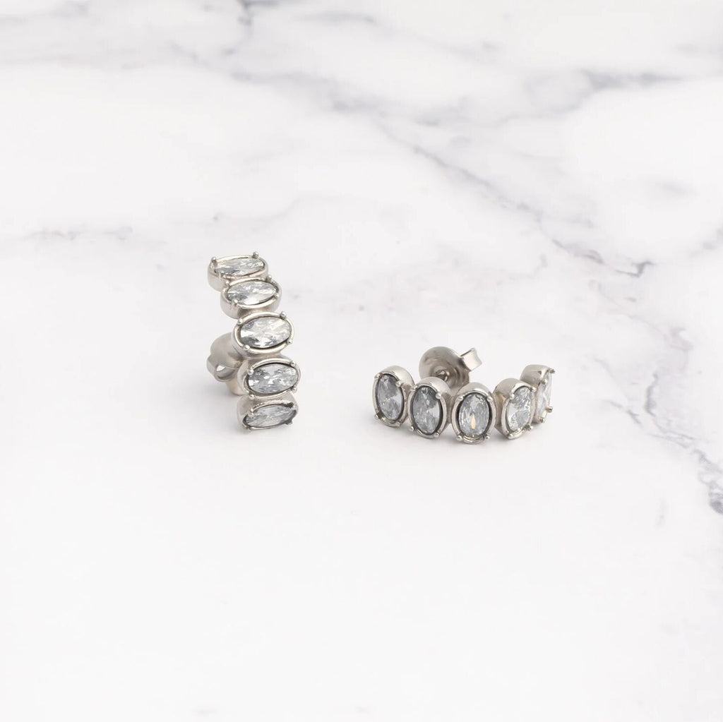 Pair of silver Oval Stone Huggie Earrings with clear stones on a marble surface