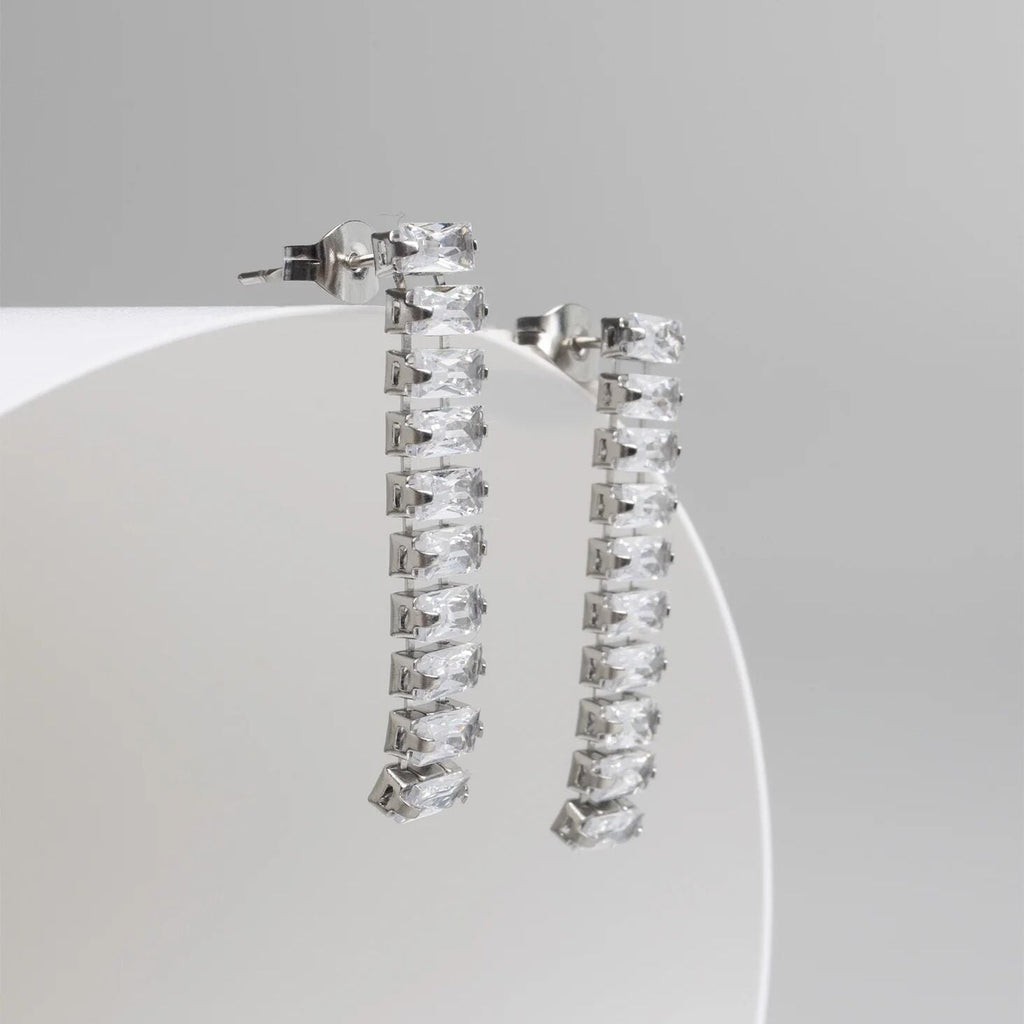Silver hoop earrings with clear gemstones on a white stand against a gray background