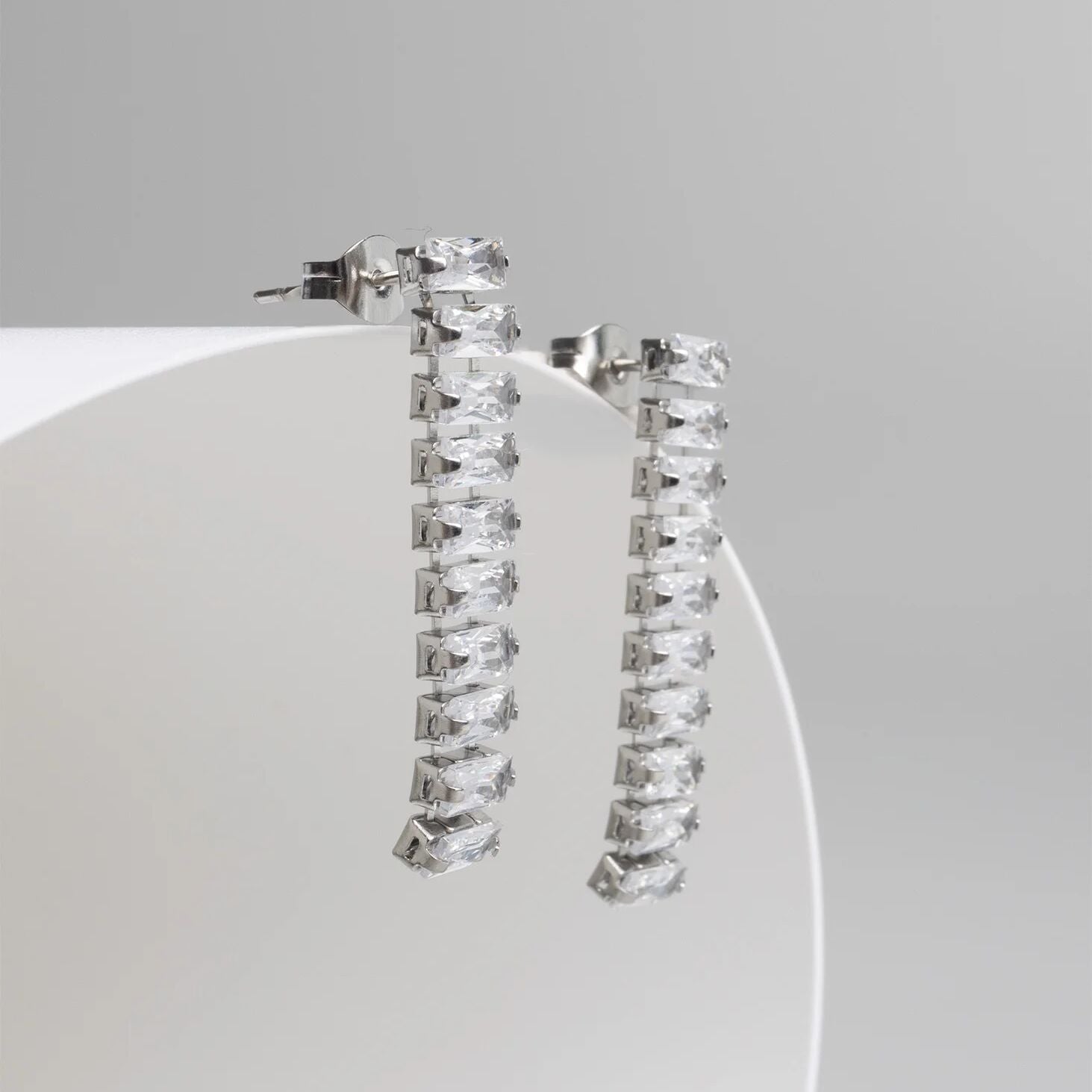 Silver hoop earrings with clear gemstones on a white stand against a gray background