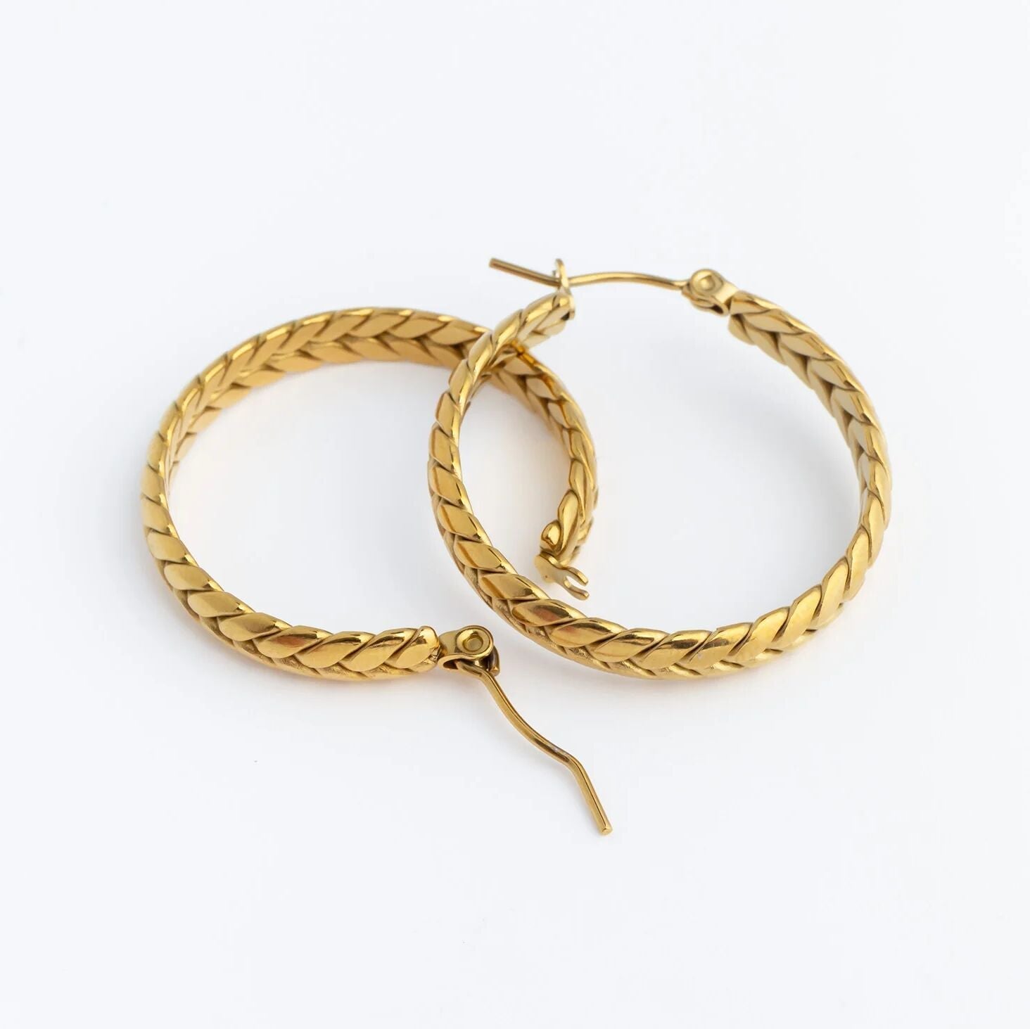 Gold hoop earrings with braided design on a white background