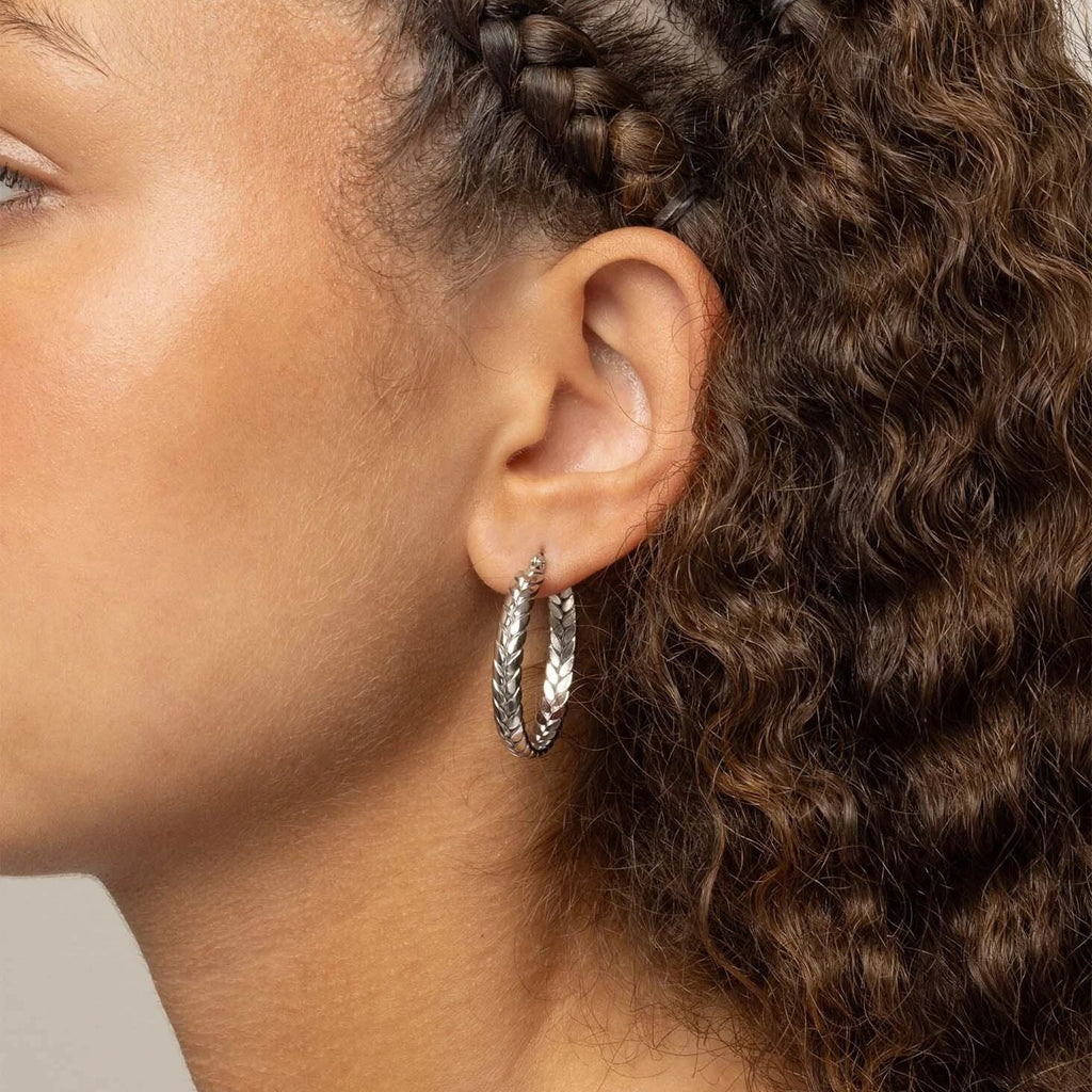Close-up of an ear wearing a silver hoop earring with braided hair.
