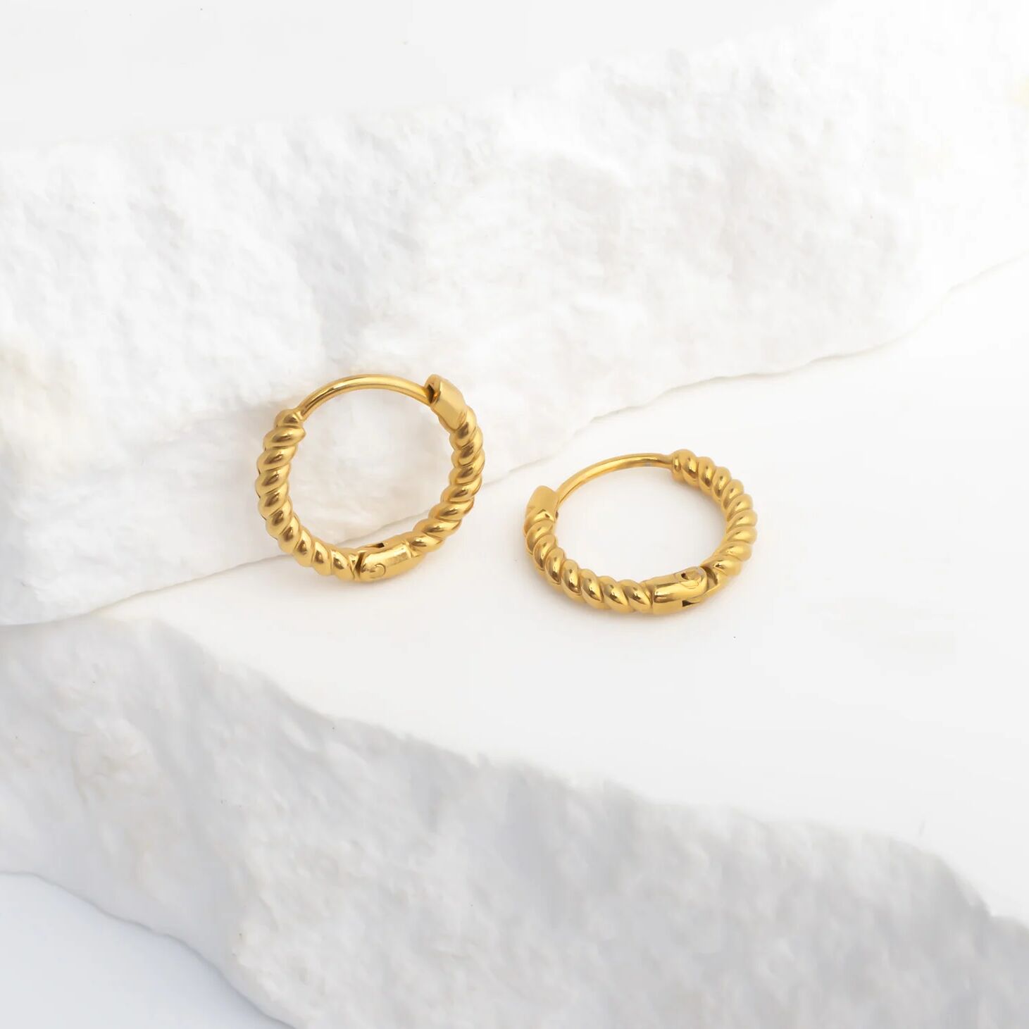 Gold hoop earrings on a white fabric background