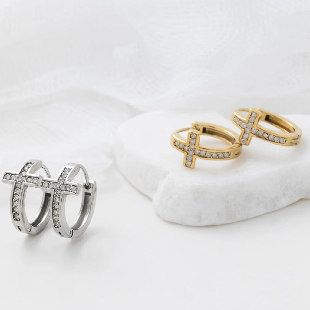 Pair of silver hoop earrings and gold cross-shaped rings on a white surface