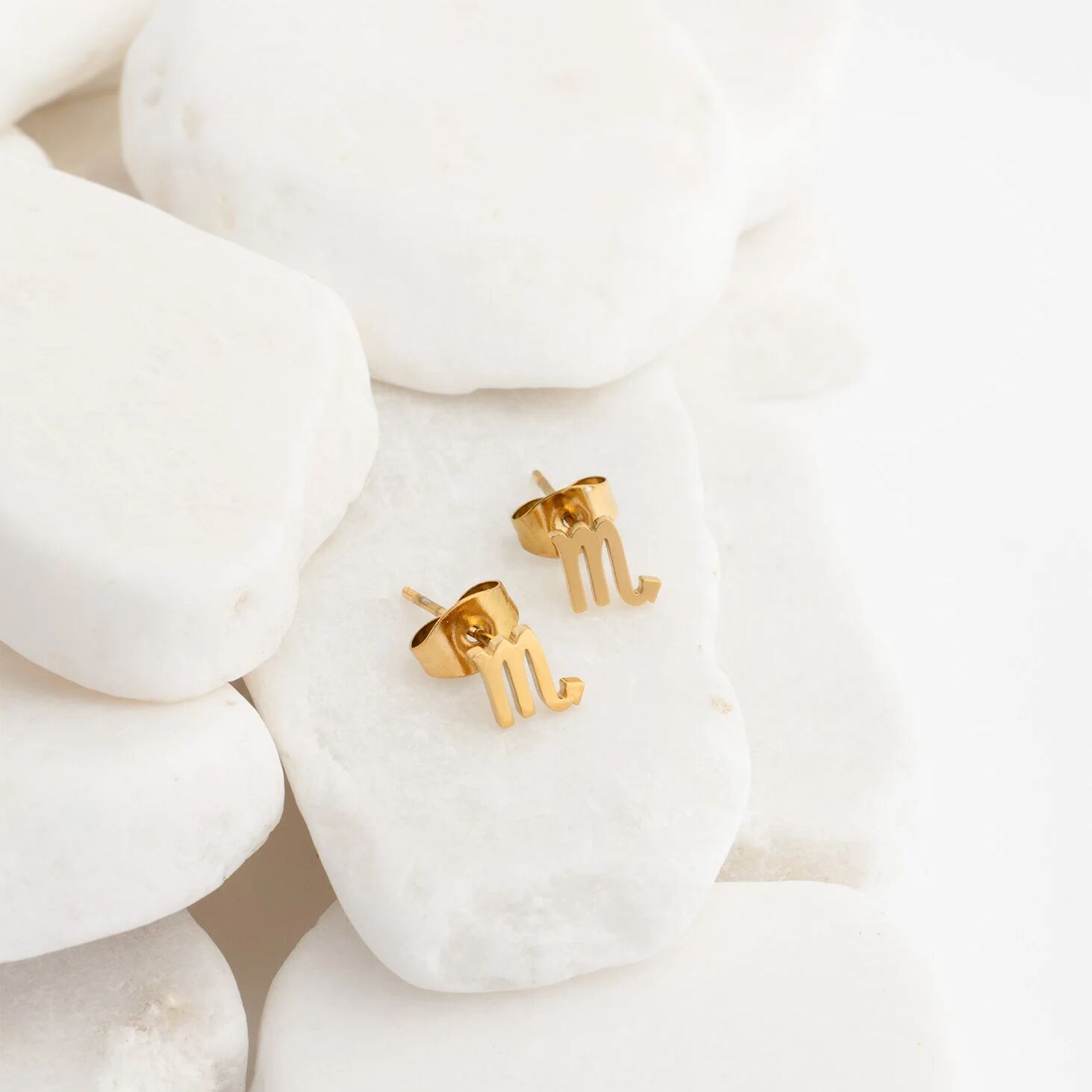 Gold letter earrings on a white stone background