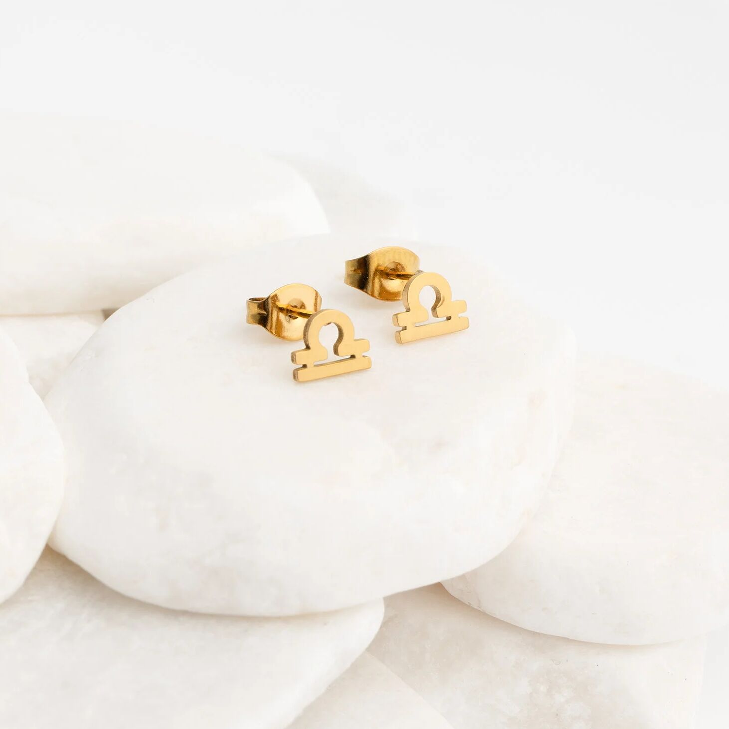 Gold Libra zodiac stud earrings on a white background