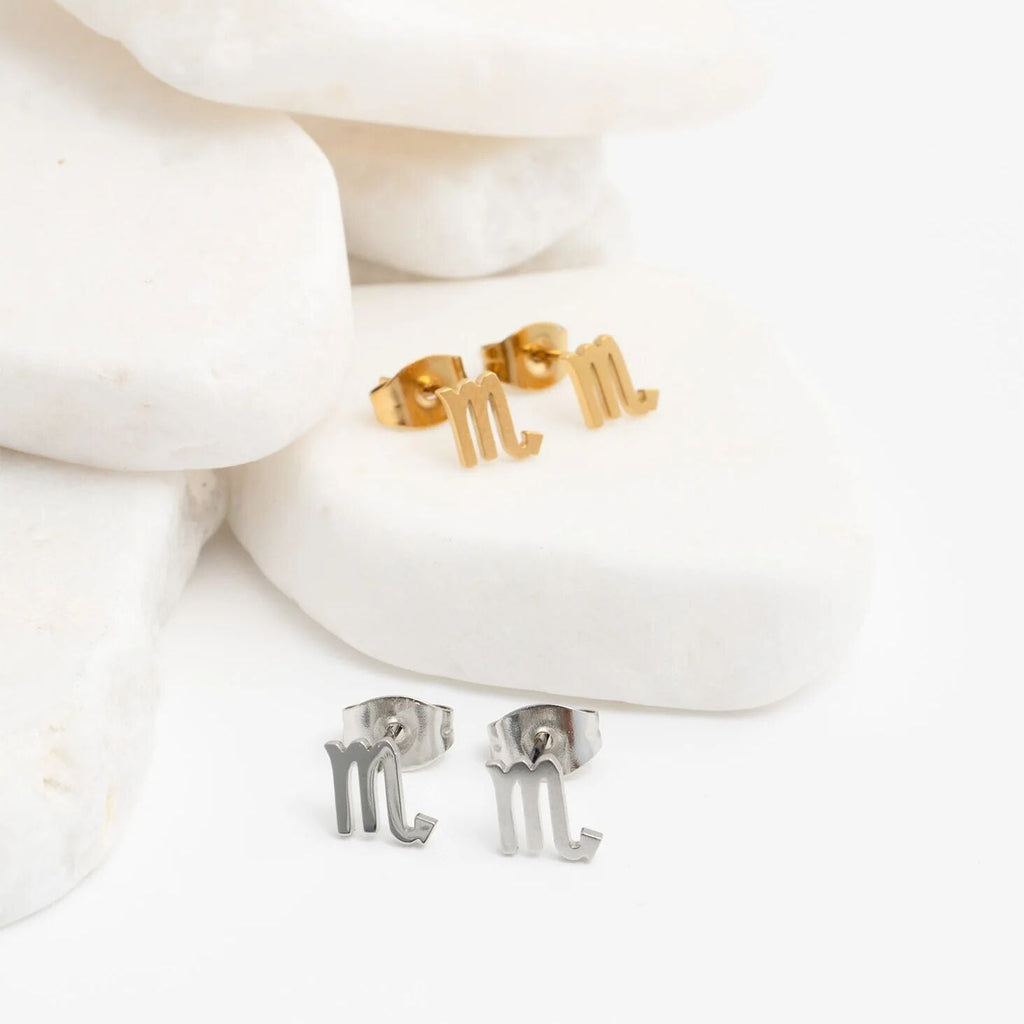 Gold and silver Zodiac Scorpio earrings on a white stoned background
