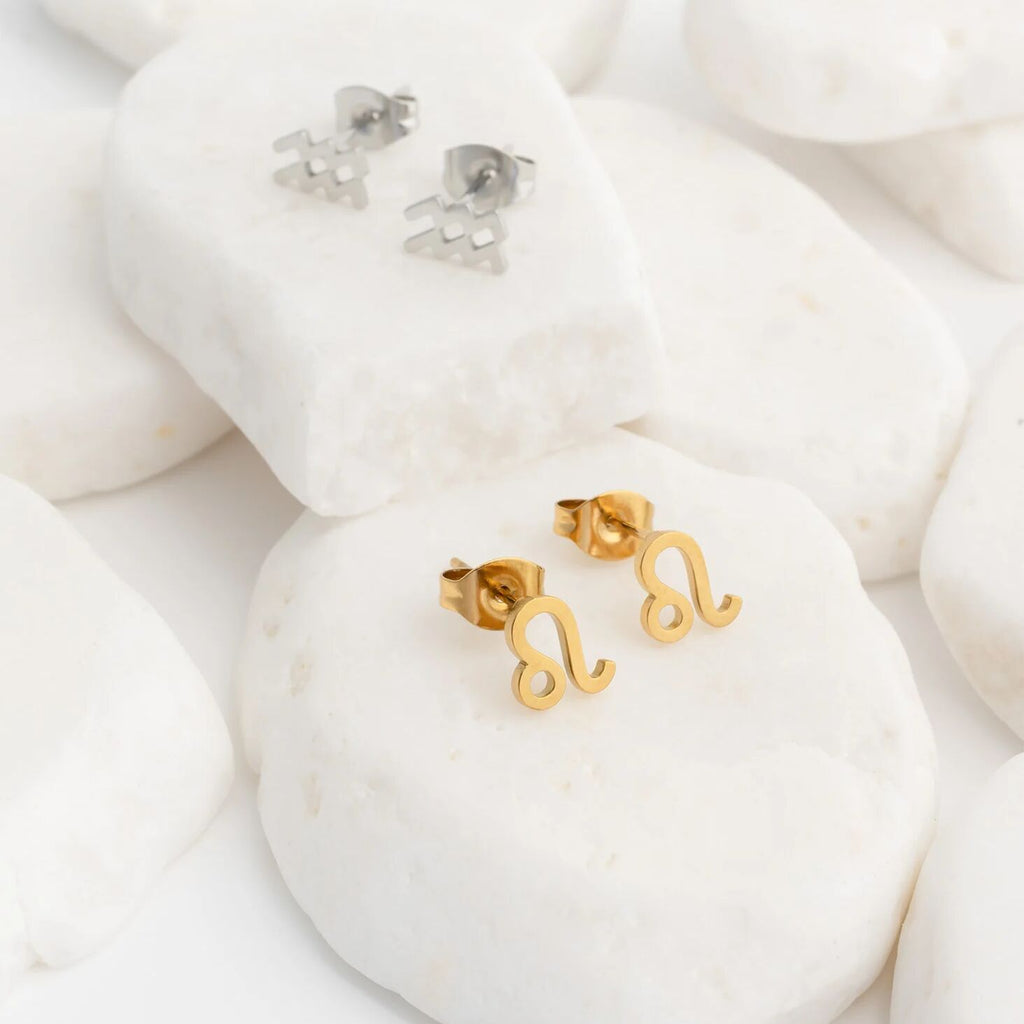 Gold Zodiac Leo earrings on a white stone surface