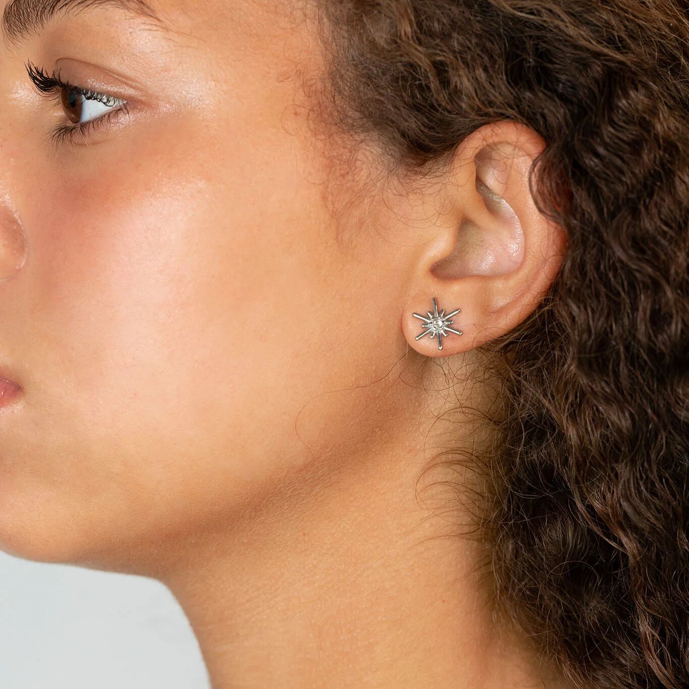 Close-up of a person wearing a firework earring with a neutral background