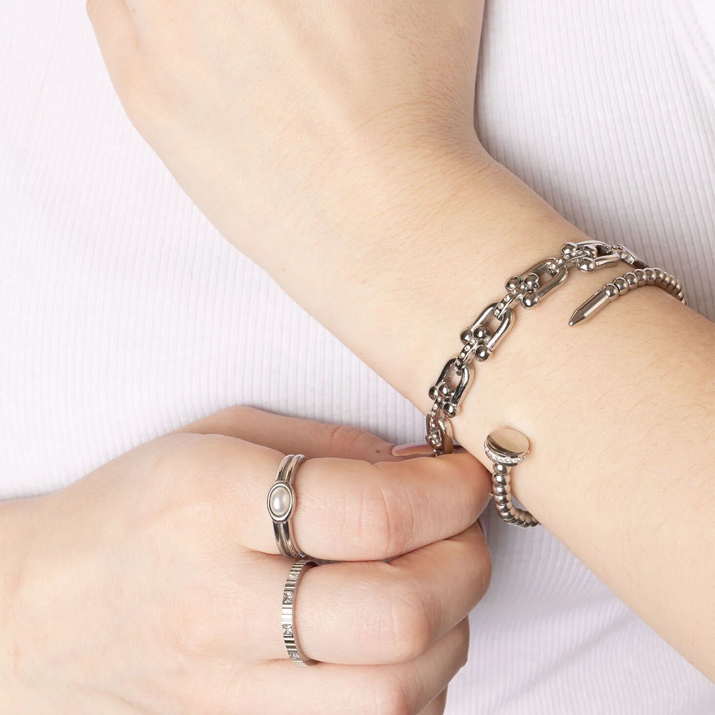 Close-up of a wrist with multiple silver bracelets and rings on a white background