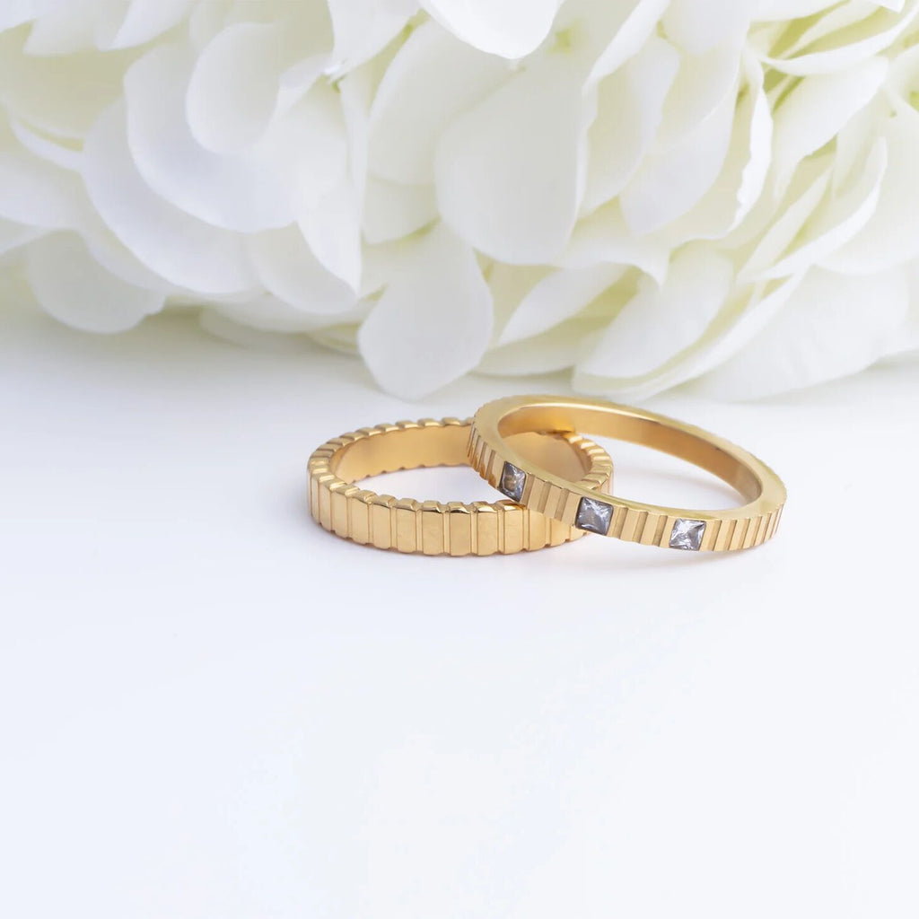 Two gold rings with diamond accents on a white background with white flowers.