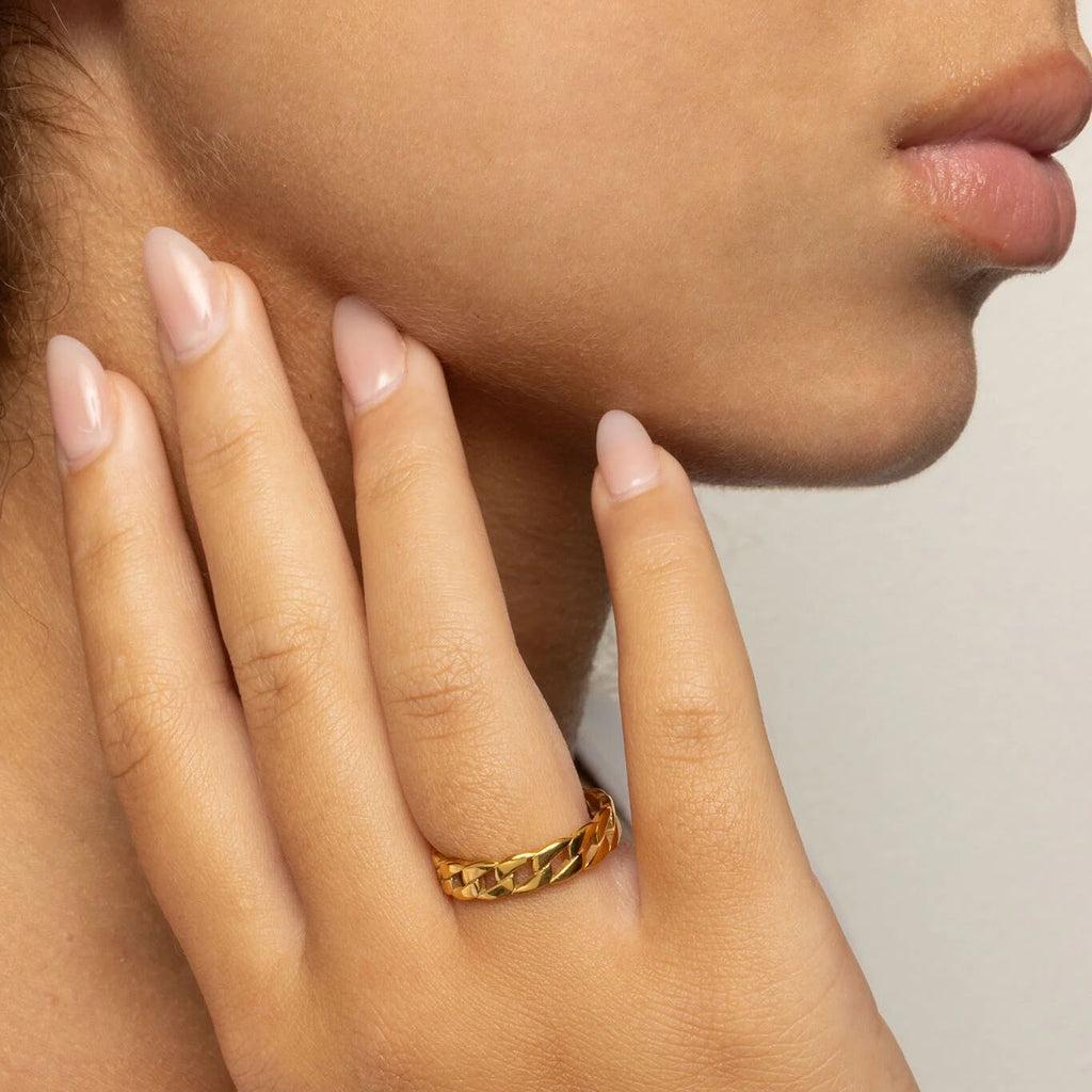 Close-up of a hand wearing a gold ring with a neutral background