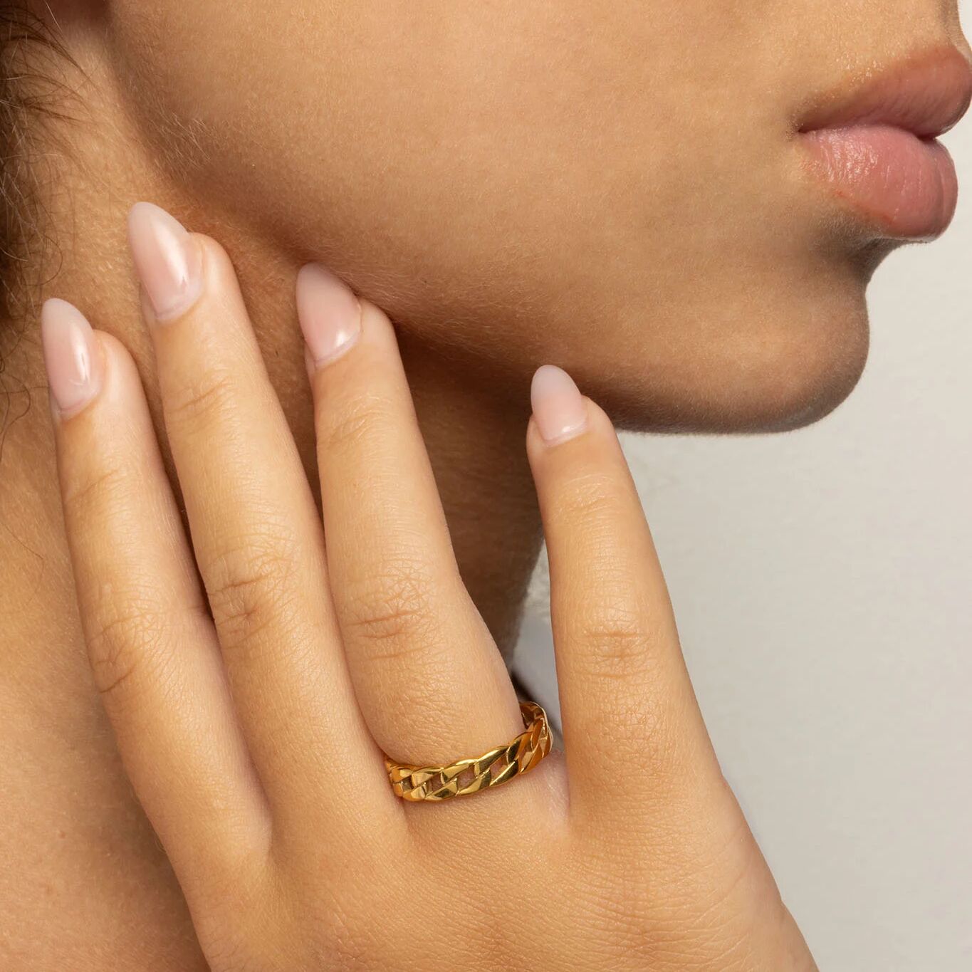 Close-up of a hand wearing a gold ring with a neutral background