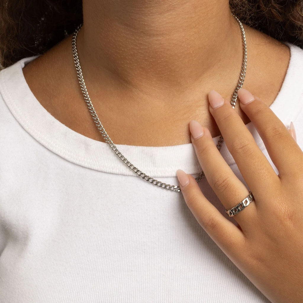 Person wearing a silver chain necklace and ring on a plain background