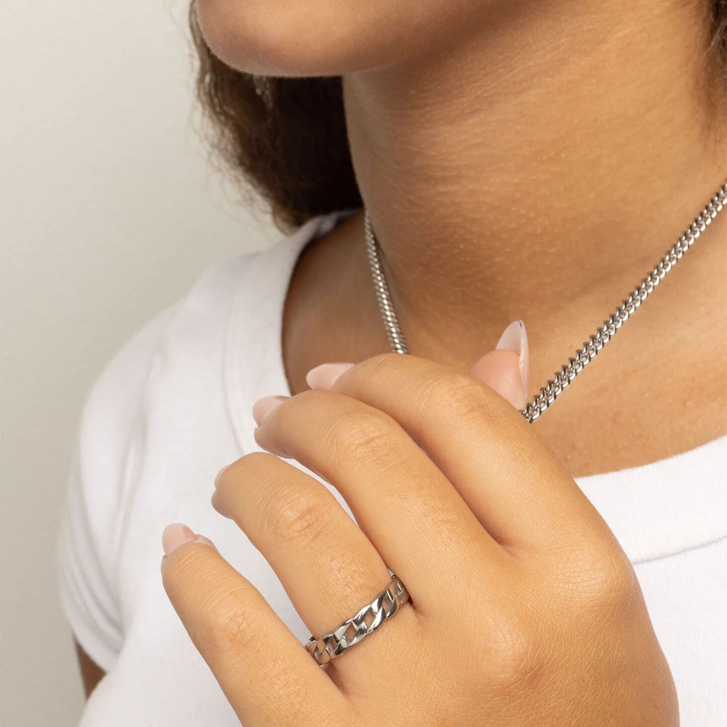 Close-up of a person wearing a silver necklace and ring on a plain background