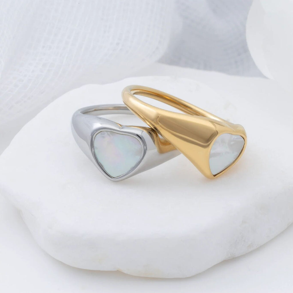 Two heart-shaped rings, one gold and one silver, on a white stone surface.