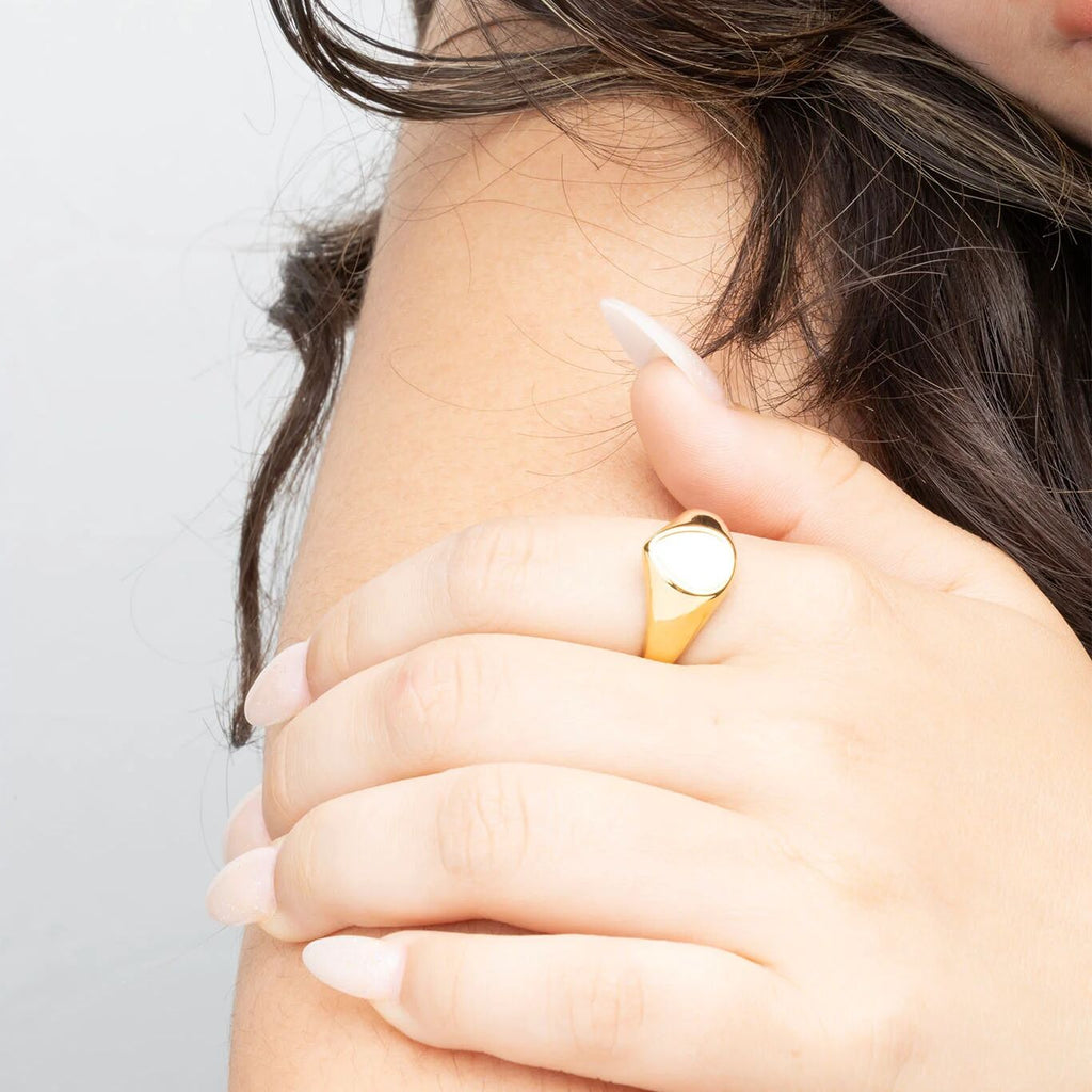 Close-up of a hand wearing a gold ring with a MOP on a neutral background