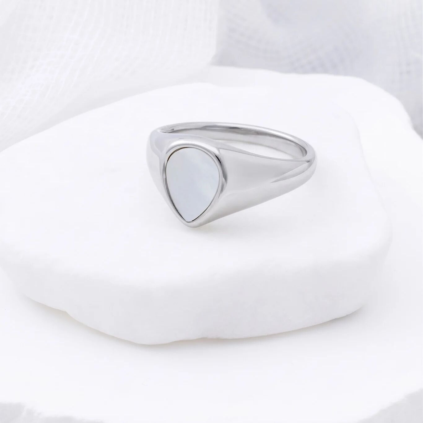 Silver signet ring on a white stone with a white background