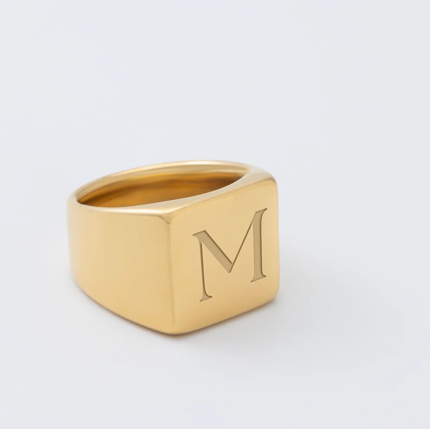 Gold square signet ring with 'M' on a light gray background