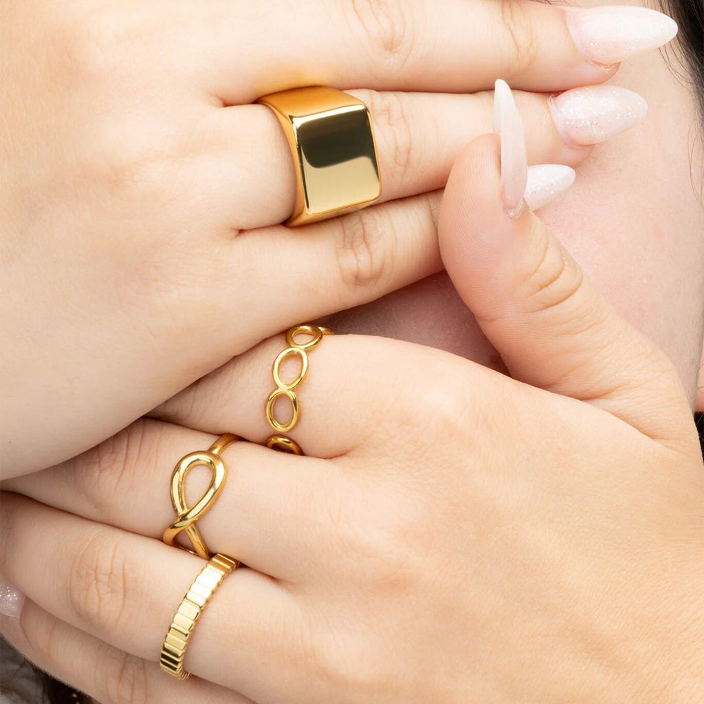 Close-up of hands wearing gold rings on a neutral background