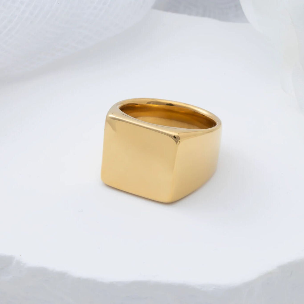 Gold square signet ring on a white fabric background