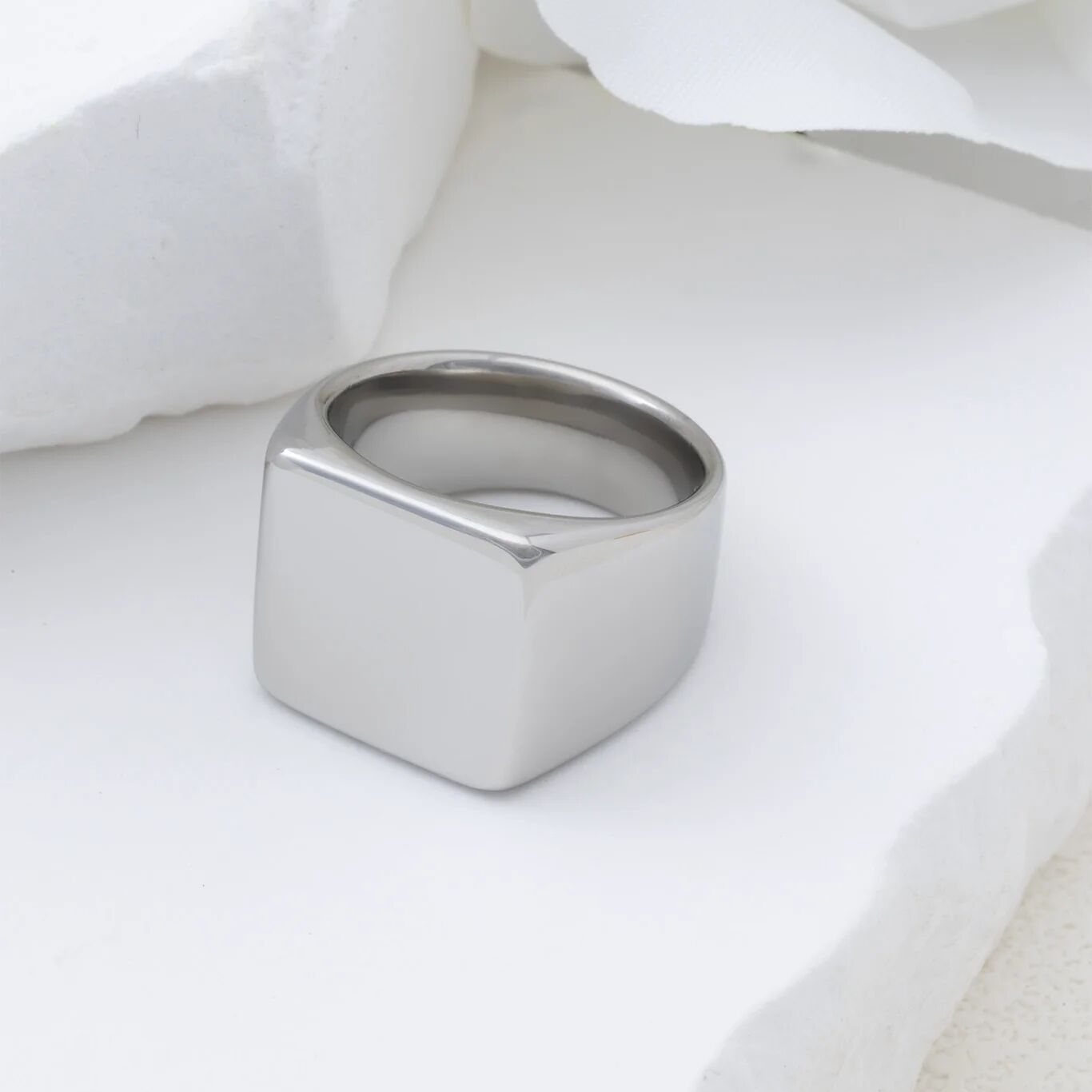 Silver square signet ring on a white fabric background