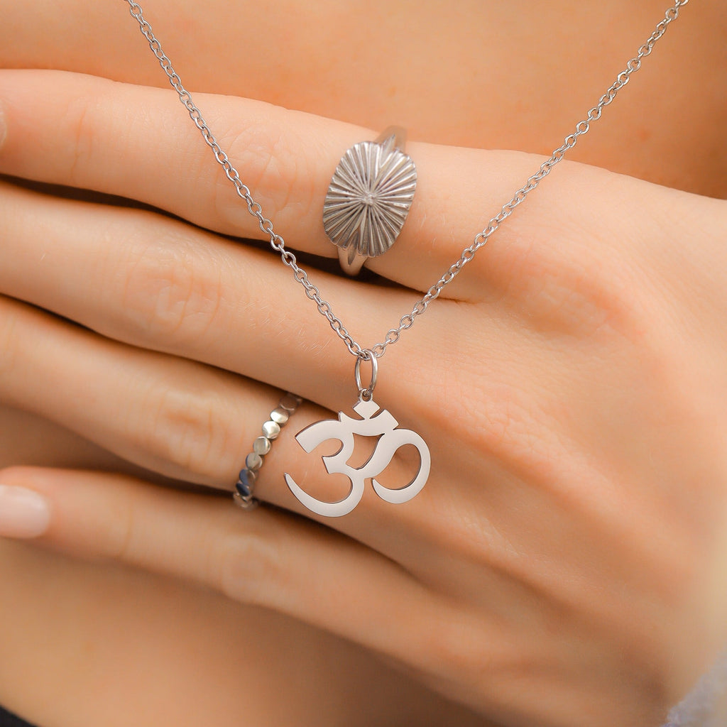 Hand wearing a silver ring with a sun design and a necklace with an Om symbol pendant.