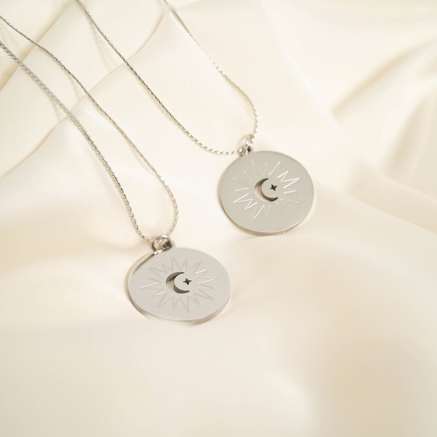 Two silver necklaces with circular pendants on a beige fabric background