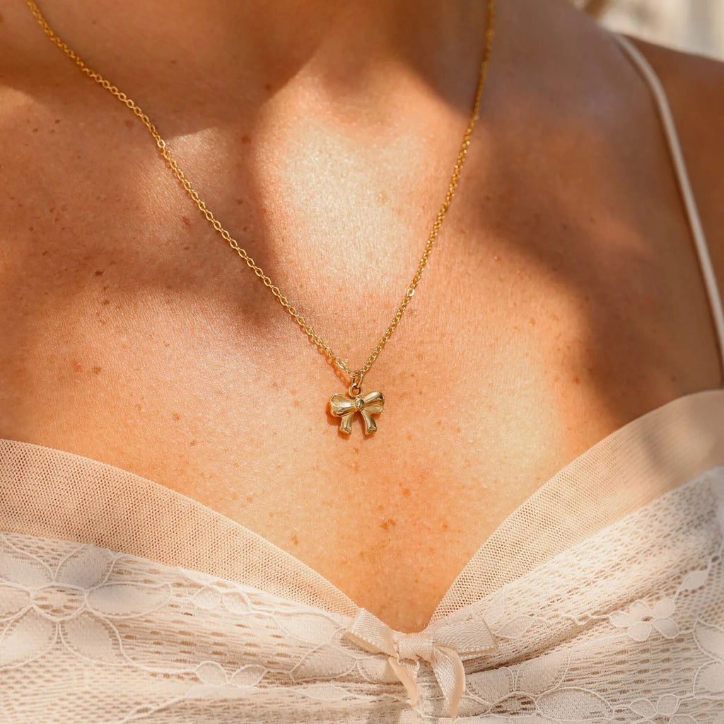 Gold necklace with a bow pendant on a person wearing a beige top.