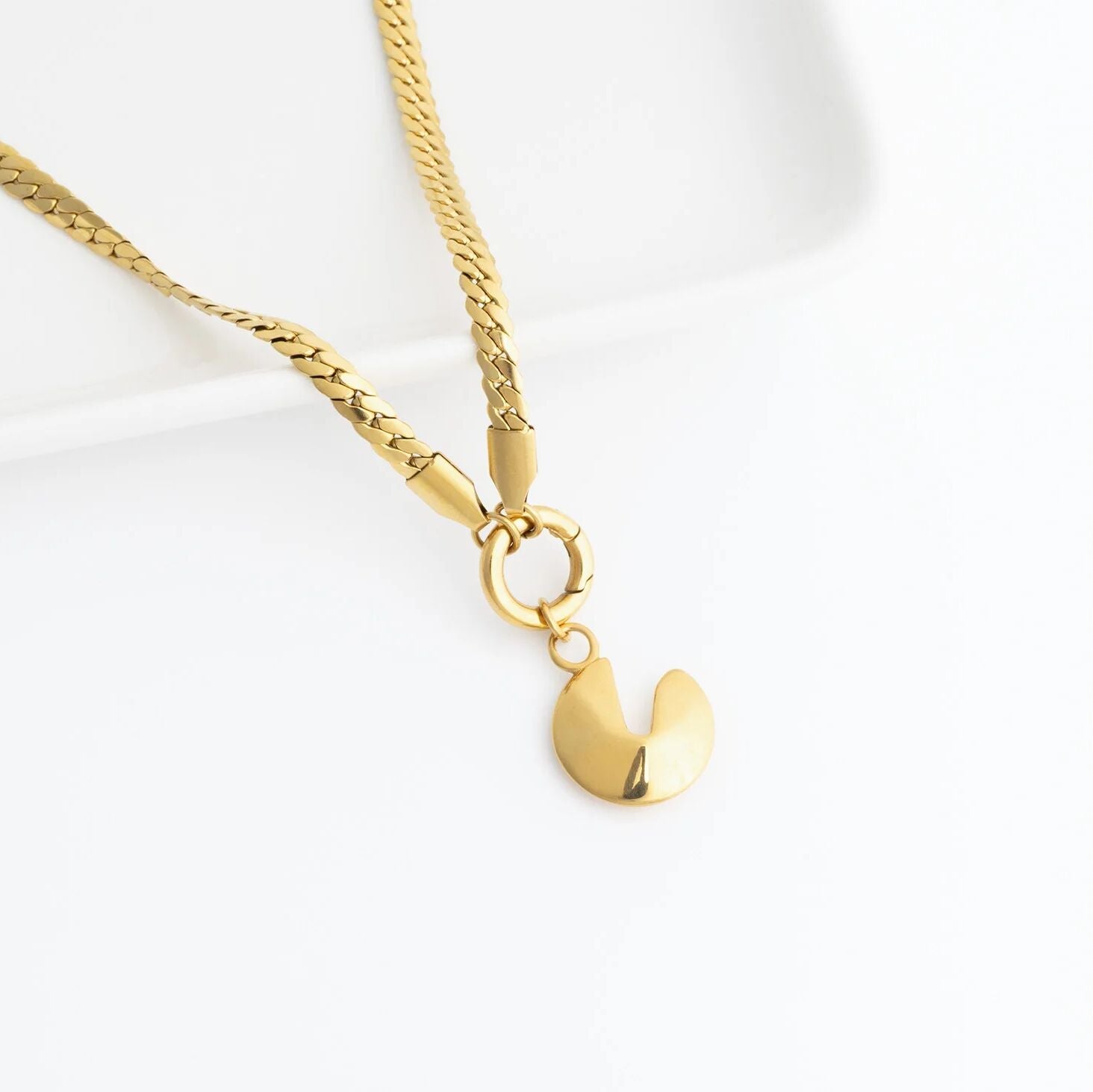Gold necklace with a fortune cookie pendant on a white background