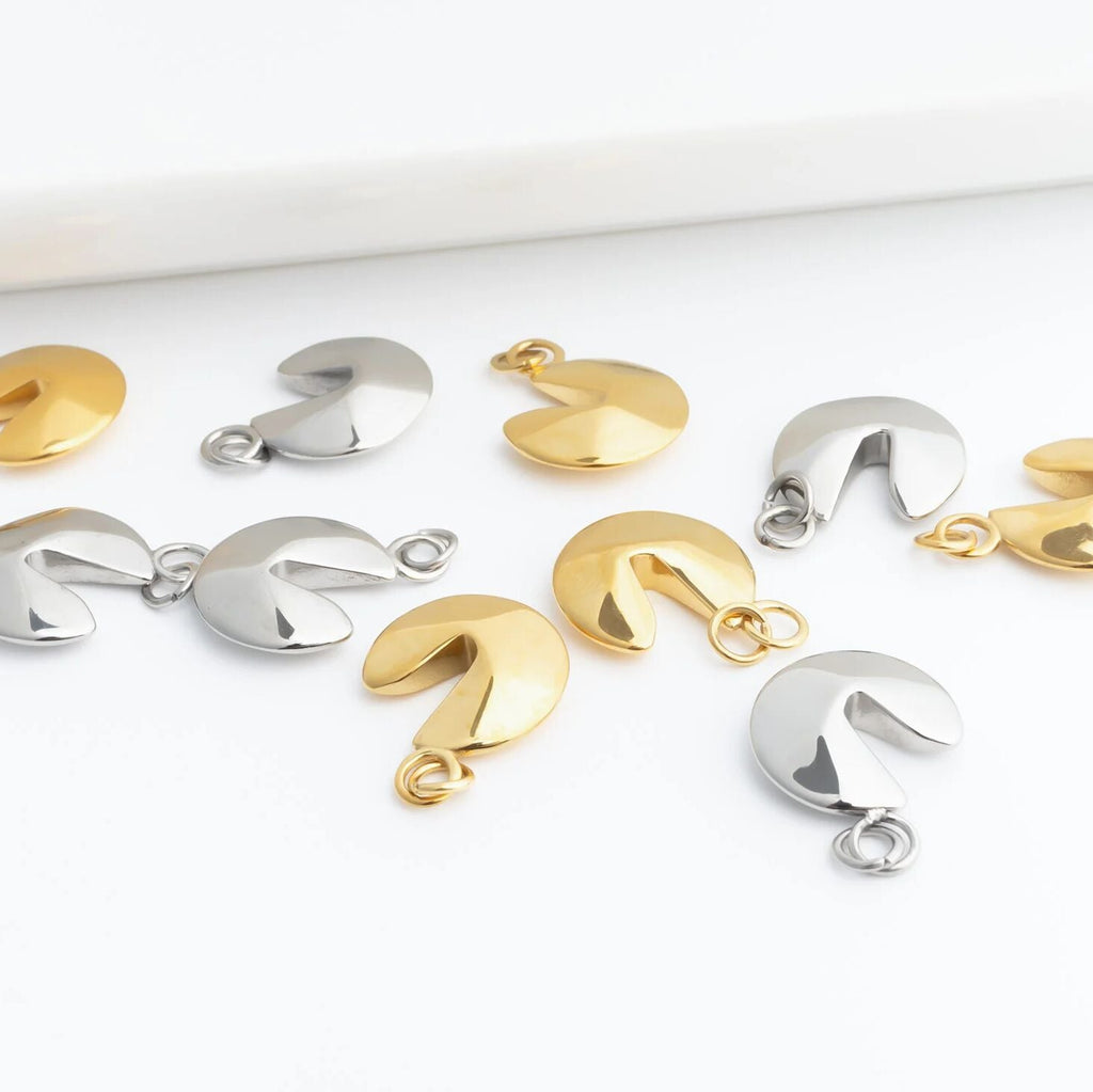 Gold and silver fortune cookie charms on a white surface