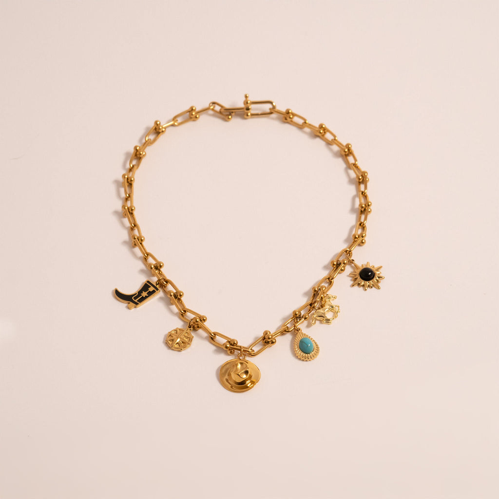 Gold charm hardware necklace with various charms including the Turquoise Tear Drop Charm on a light beige  background